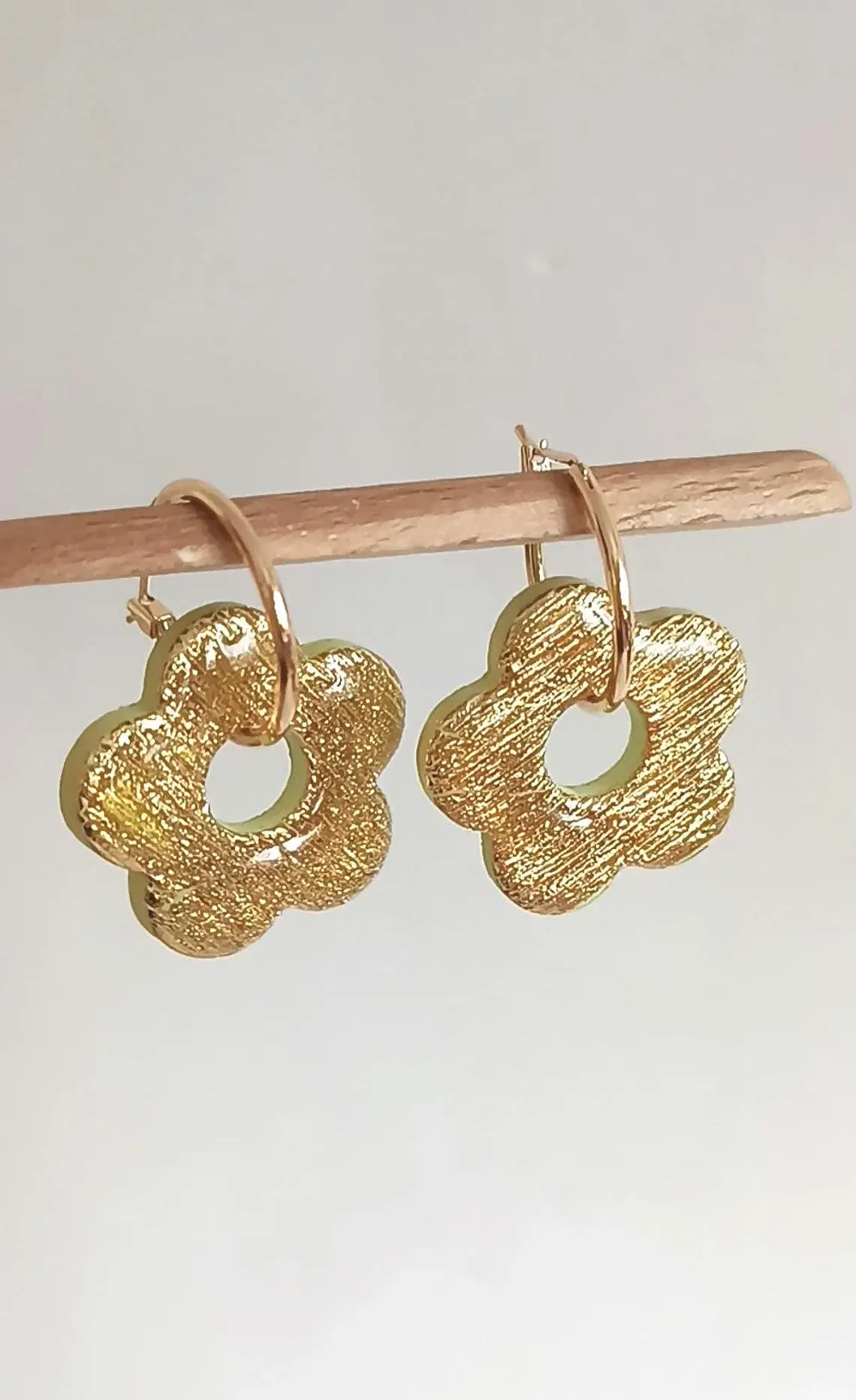 Gold hoop earrings featuring textured polymer clay flower charms. The handmade botanical dangles have a detailed surface design and hang from interchangeable gold hardware.
