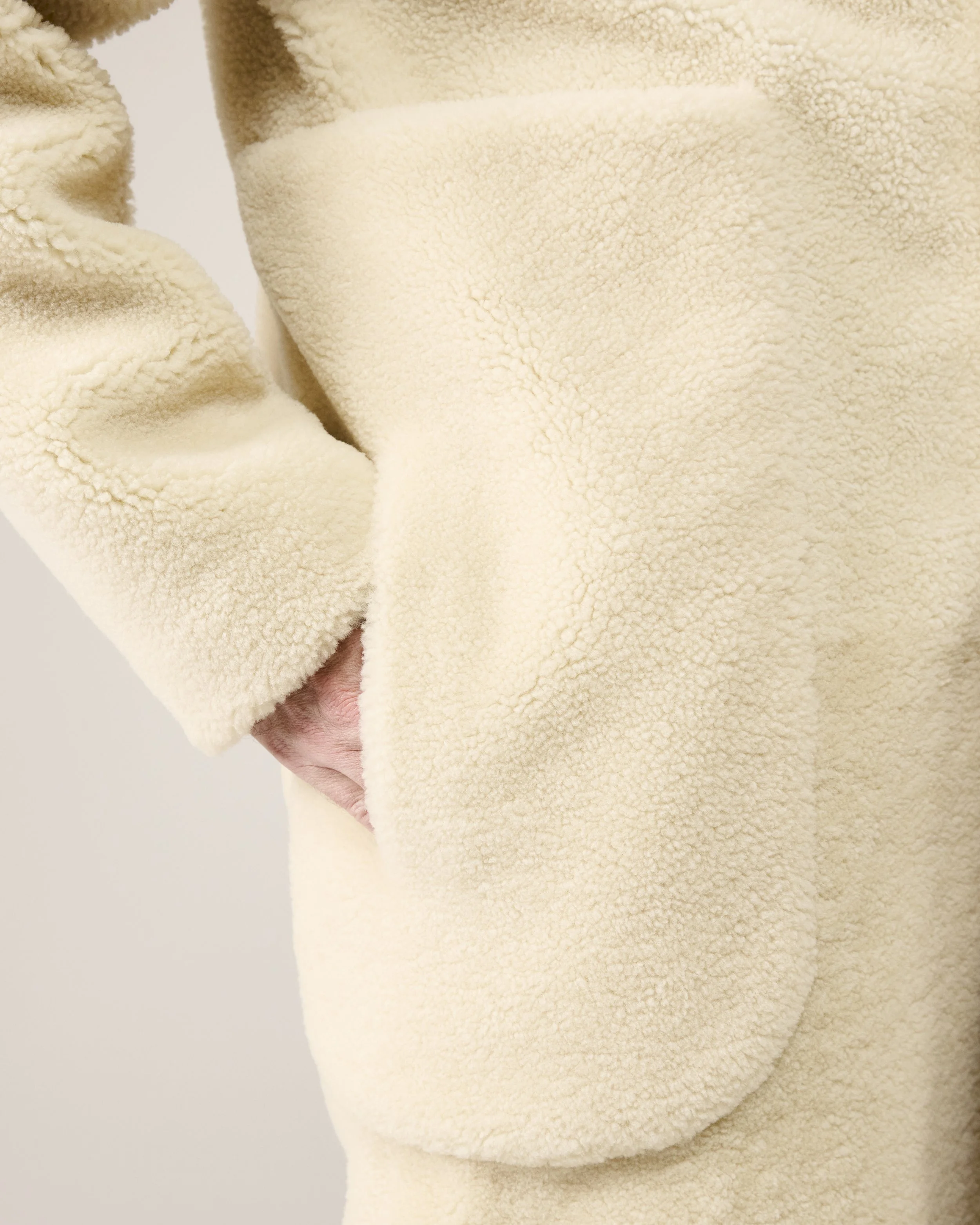 Nahaufnahme von einer Person in einem cremefarbenen, terry cloth Fleece-Pullover, die Hand steckt in der Tasche.