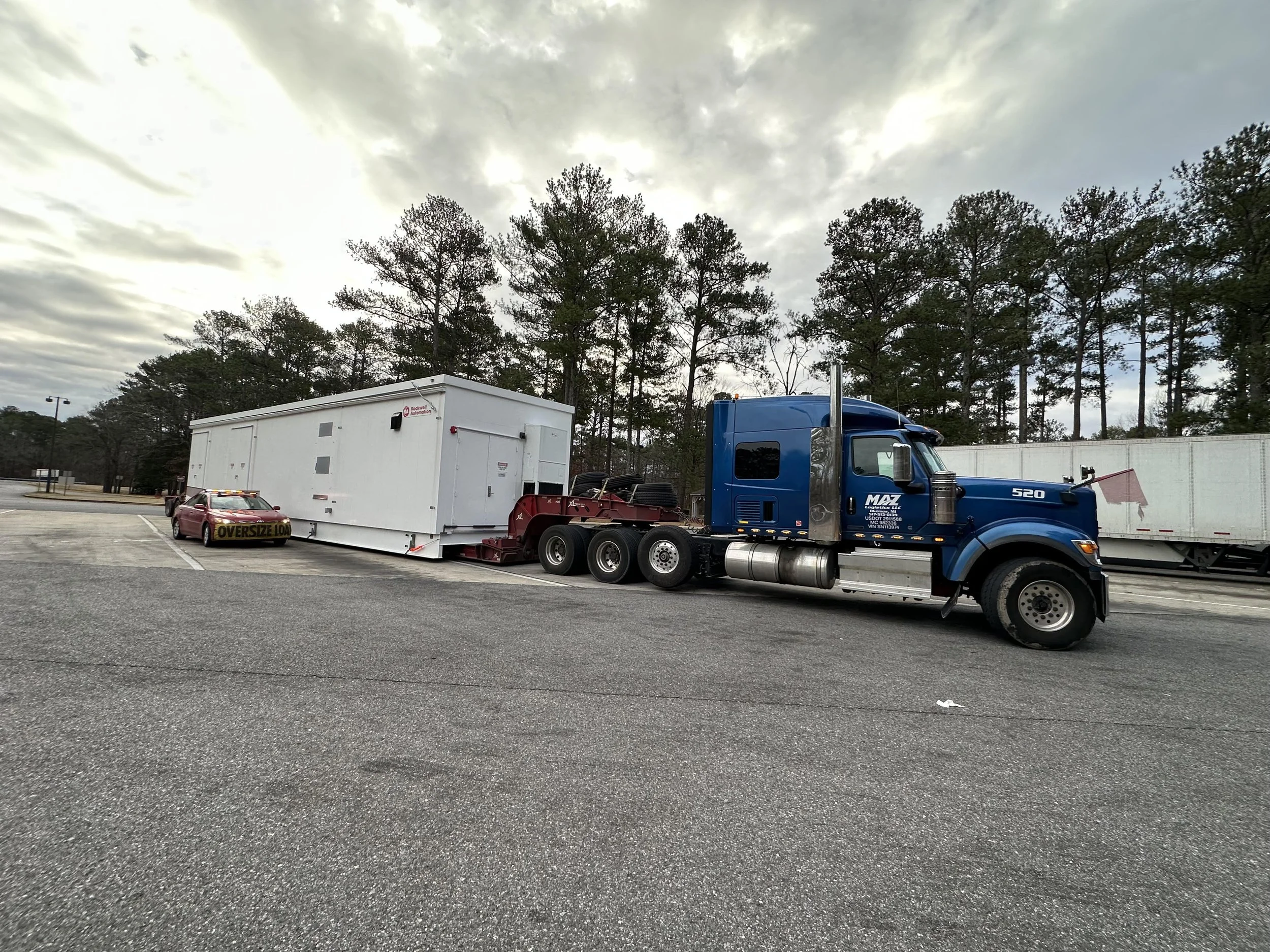 A blue semi-truck attached to a white trailer with a small white car with an 