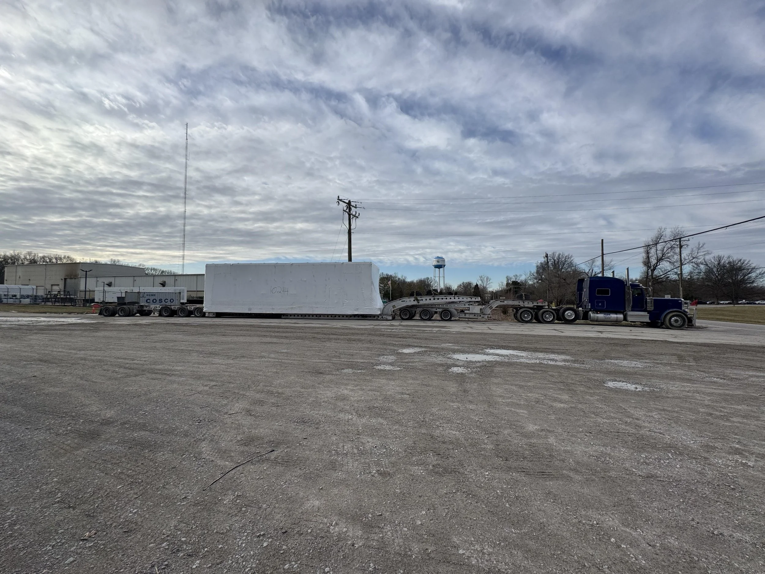 A semi-truck with a flatbed trailer parked on a gravel lot under a cloudy sky.