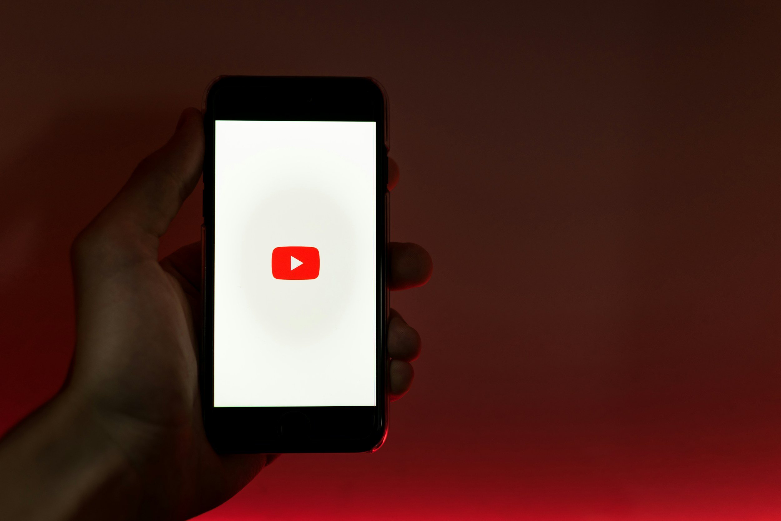 Person holding a smartphone showing the YouTube app logo on the screen.