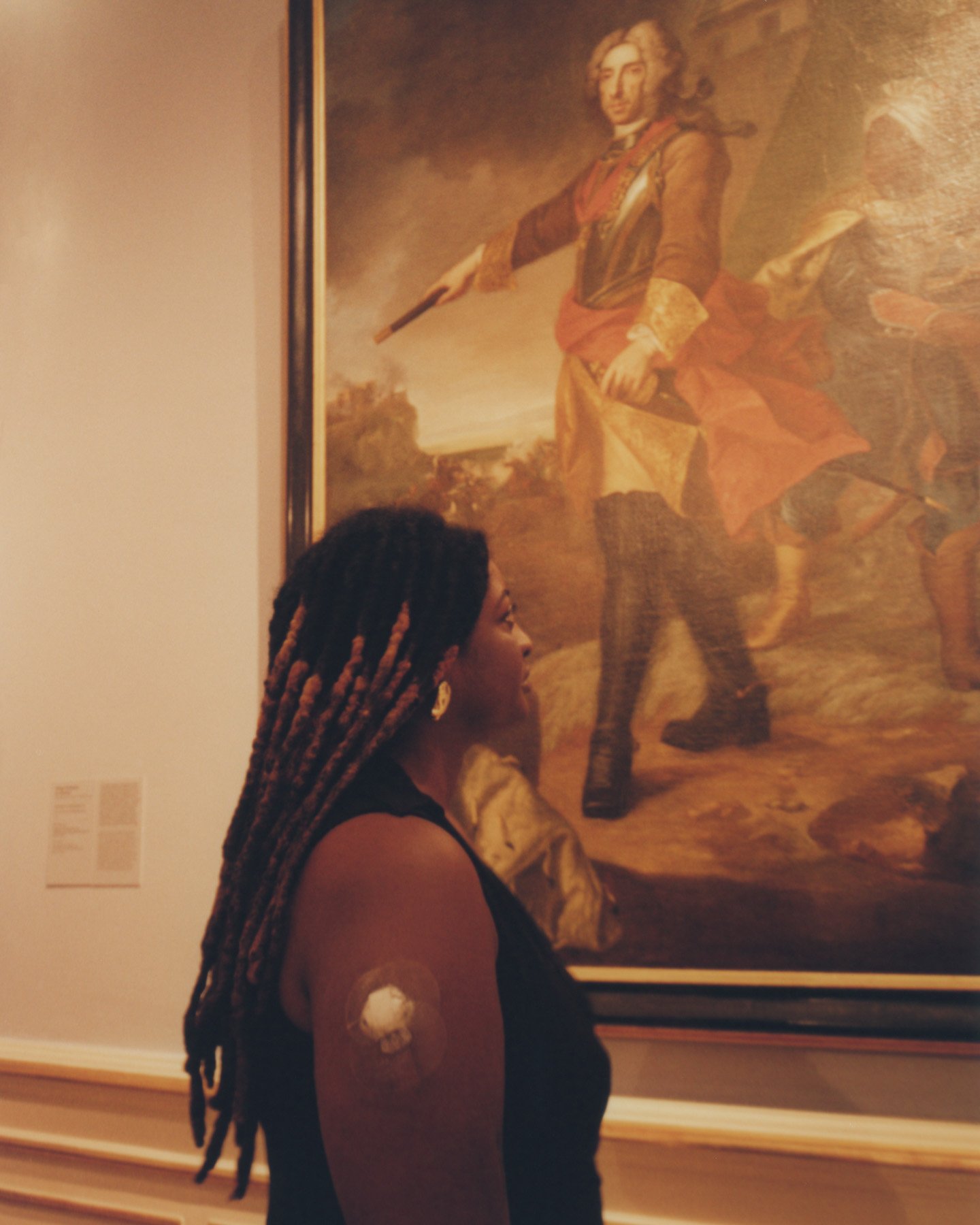 Tayla Myree with braids looking at a large historical portrait painting at an art gallery.