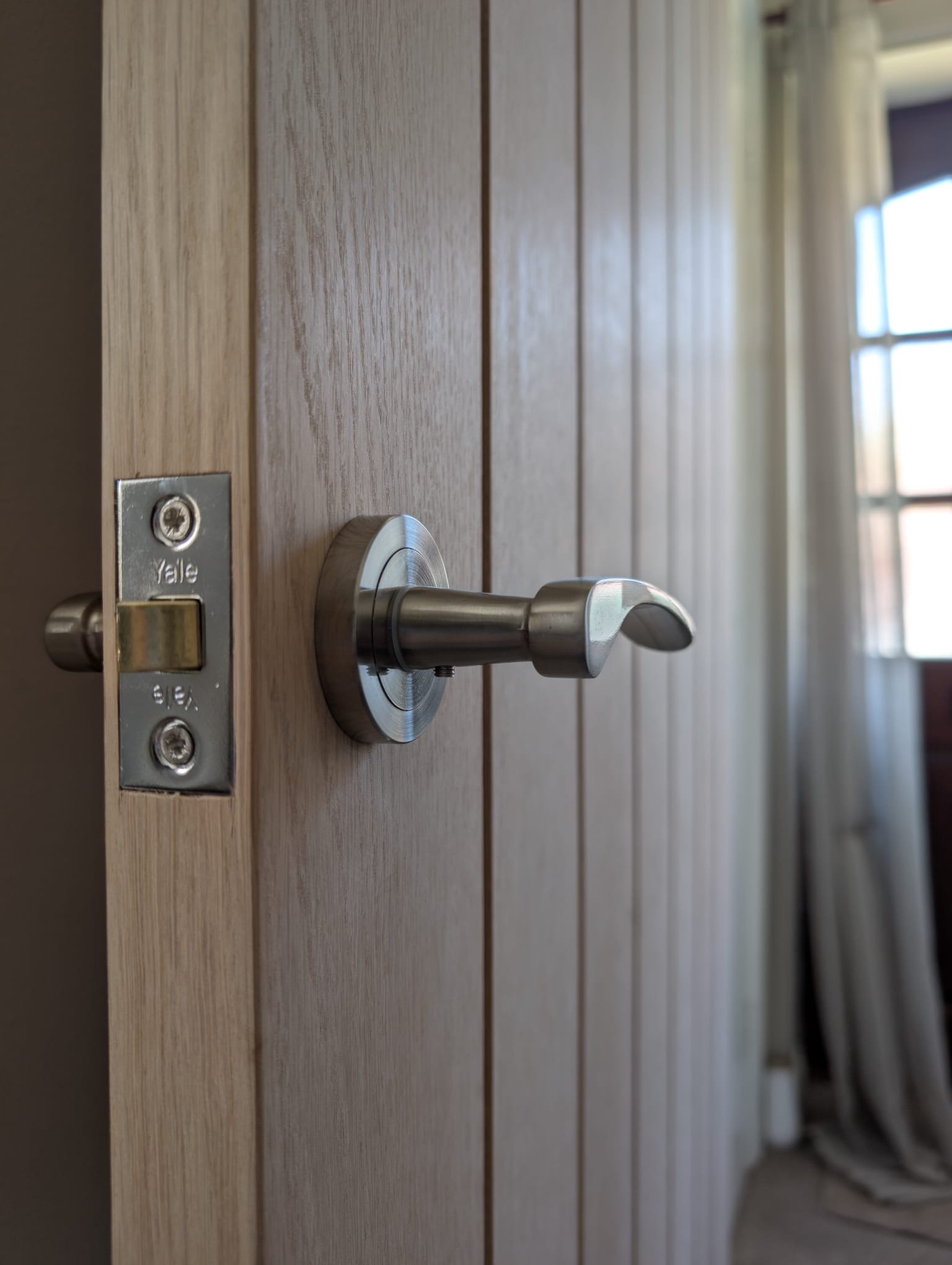 Close-up of a metal door latch with a modern, curved door handle on a wooden door.