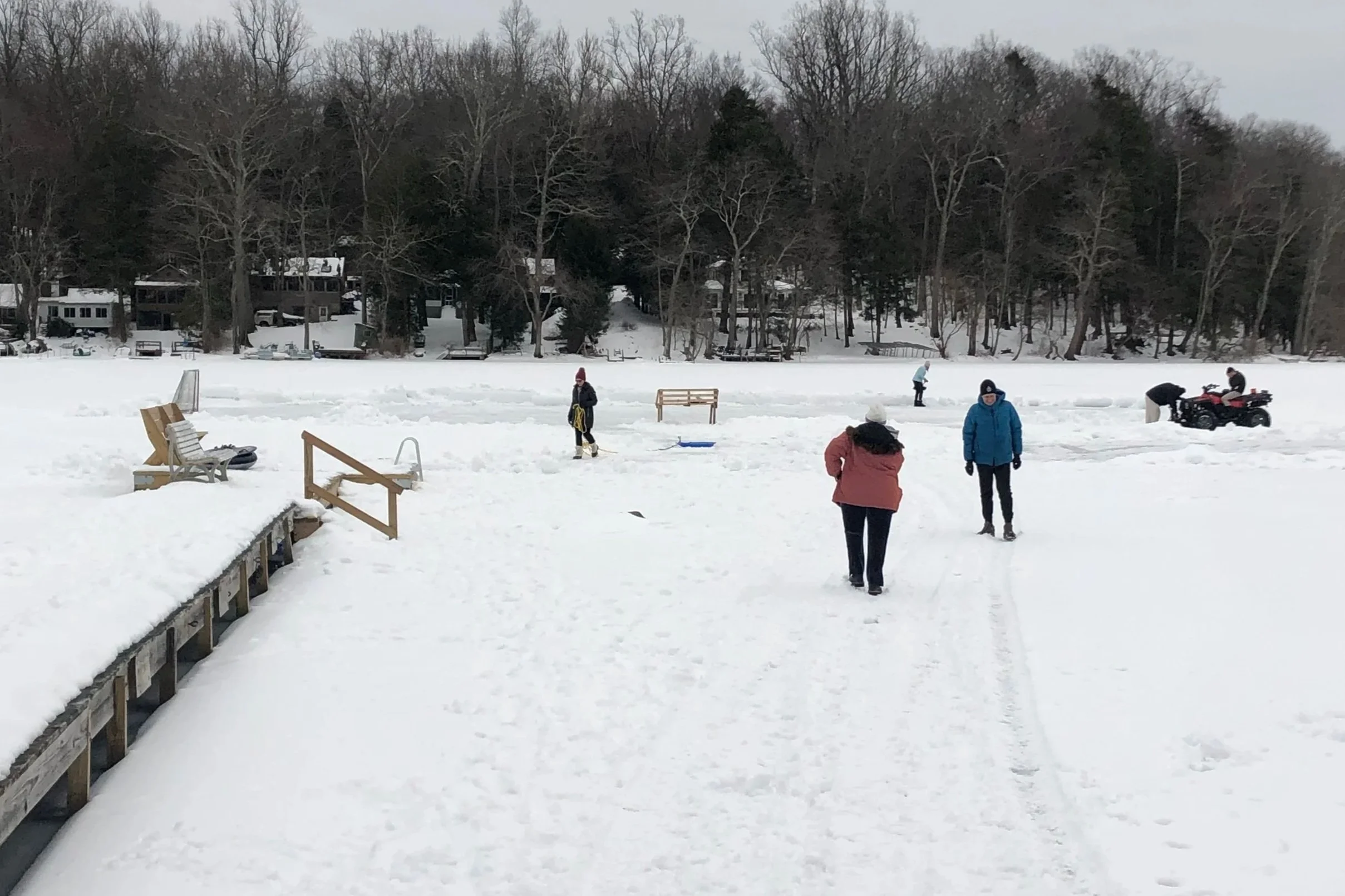 People ice skating and playing hockey on a frozen lake surrounded by snow and trees.