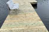 A white bench on a wooden dock beside water.