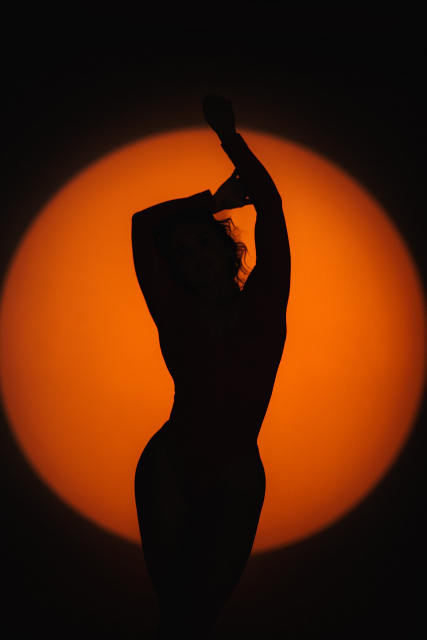 Silhouette of a person posing with arms raised and hands clasped above head against an orange sunset background.
