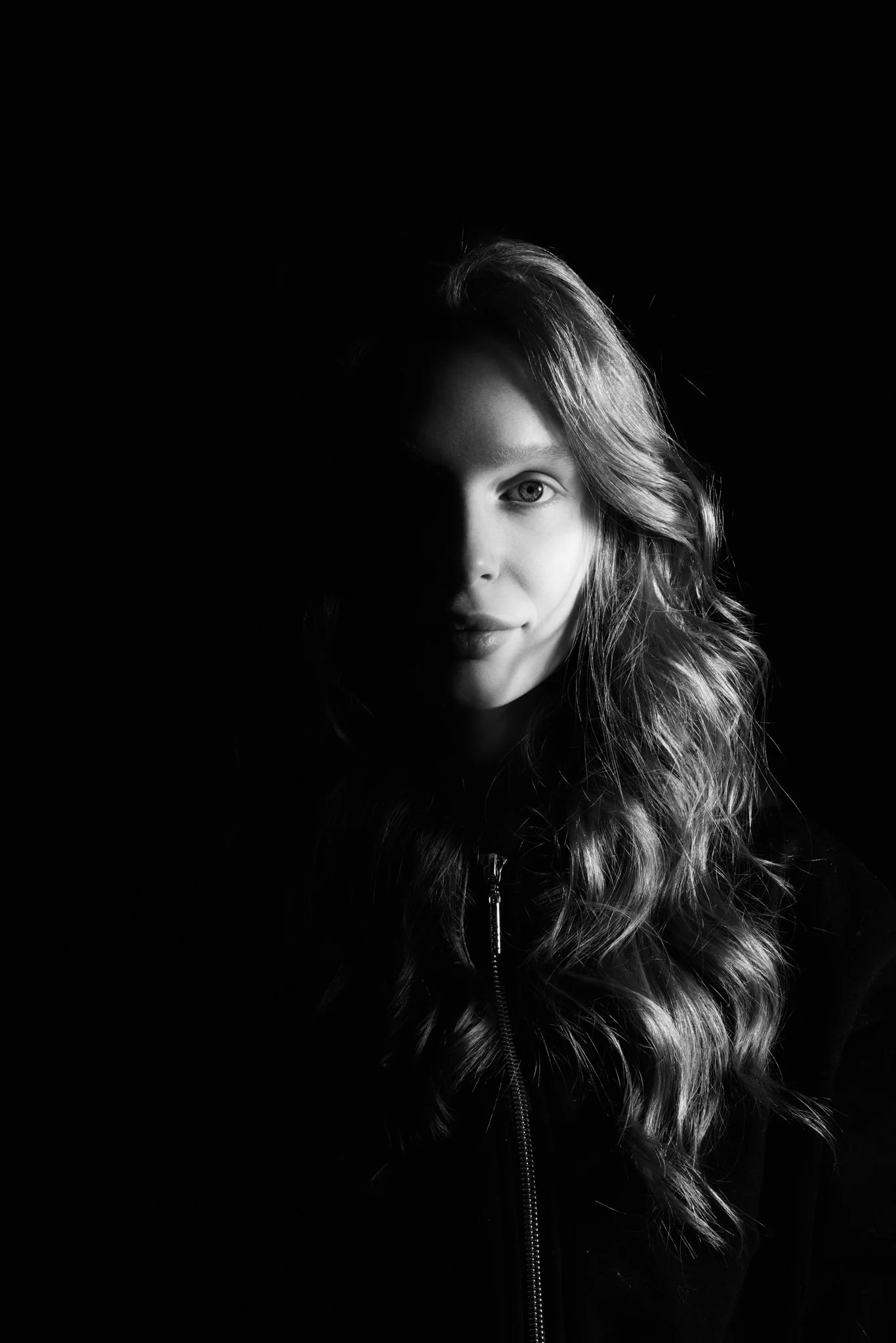 Black and white portrait of a woman with long, wavy hair, one side of her face illuminated, the other side in shadow.