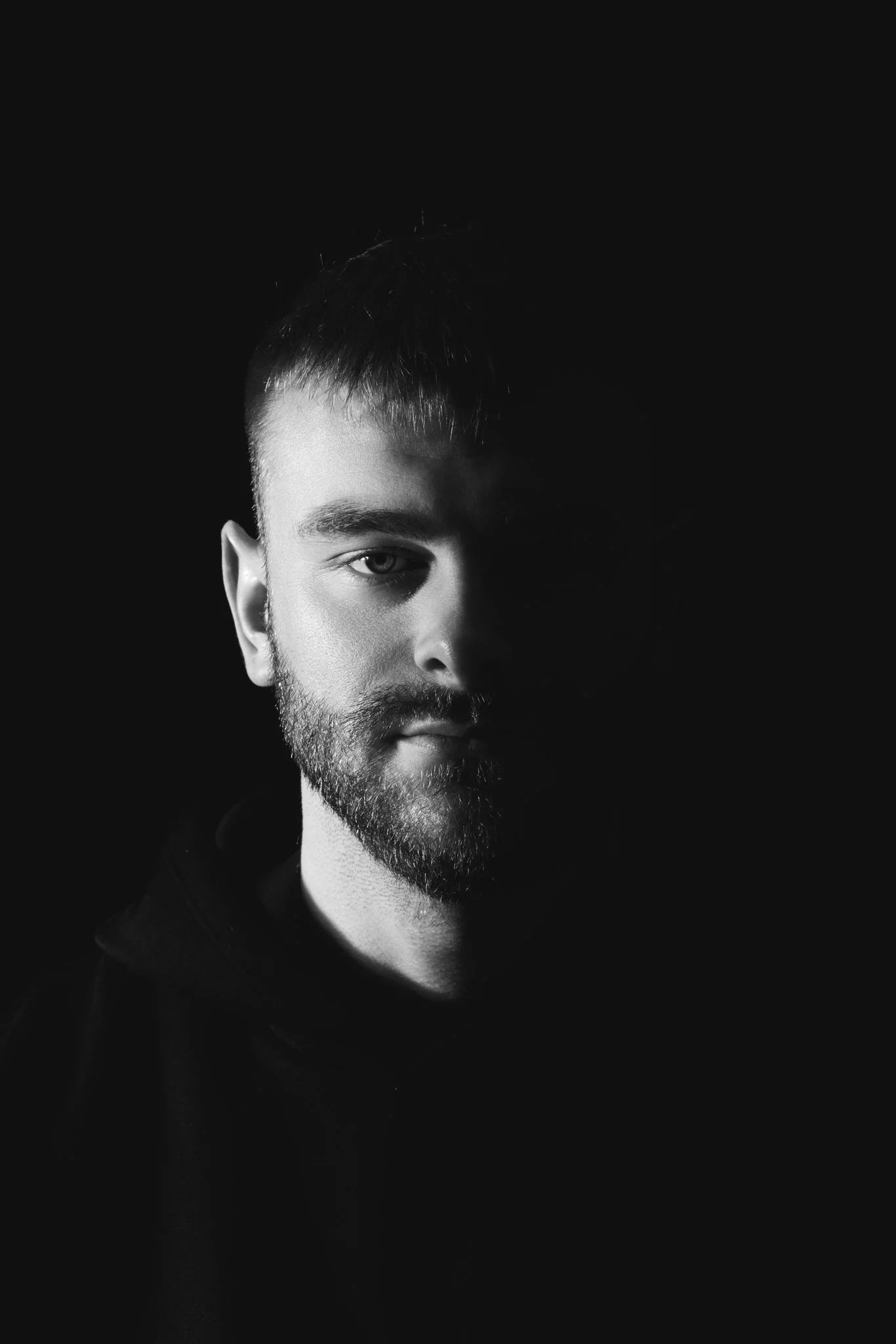 Black and white portrait of a man with one side of his face illuminated and the other side in shadow.