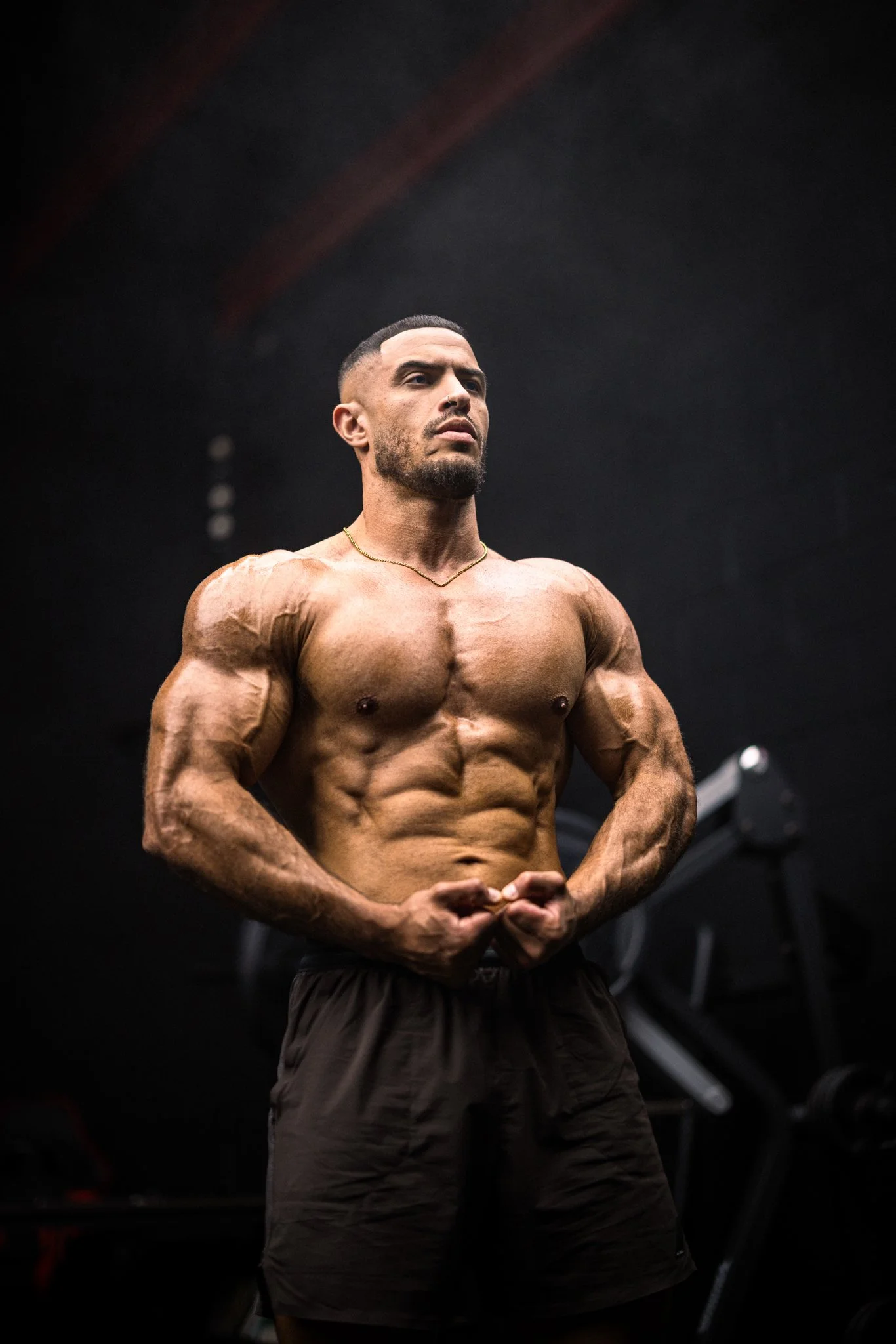 A muscular man with defined abs and arms flexes at the gym, dark background.