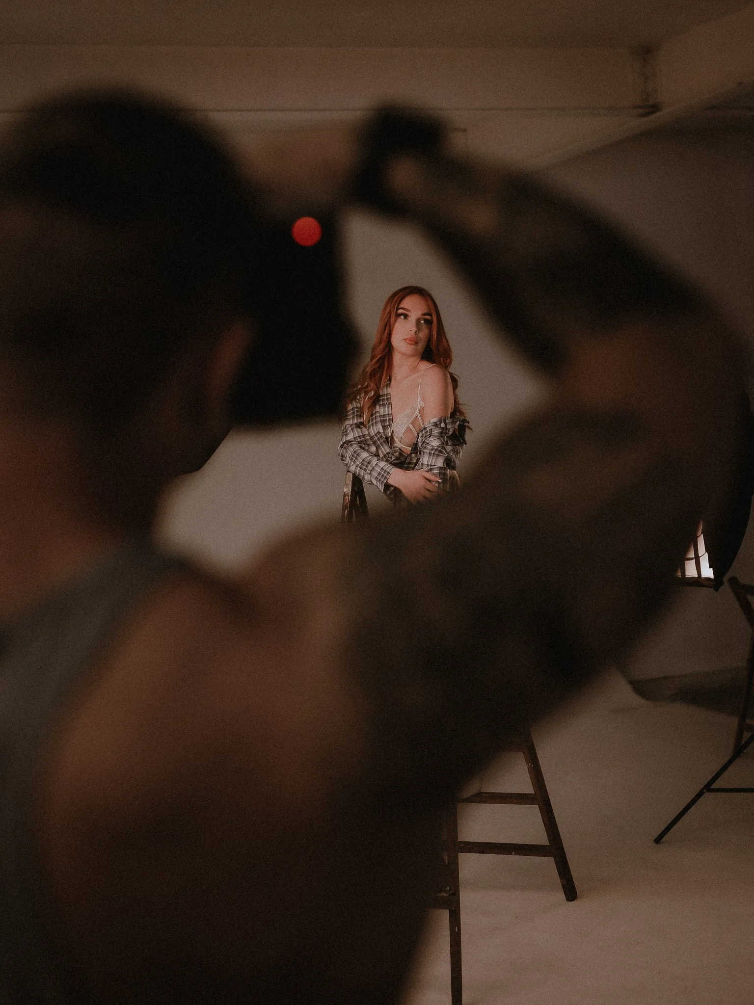 A woman with red hair posing in front of a white backdrop, seen through a blurry, dark foreground.