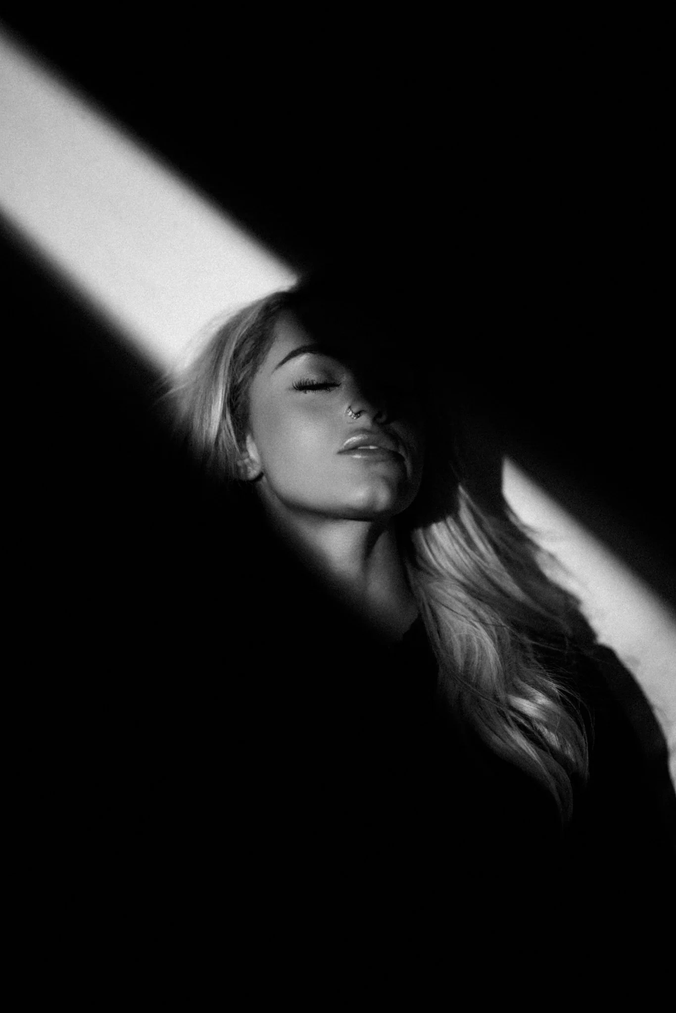 Black and white photo of a smiling woman with long hair, eyes closed, looking relaxed, with dramatic lighting and shadows.