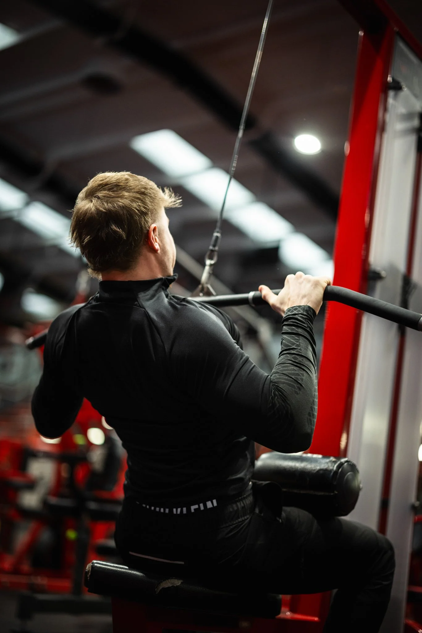 A man performing a seated lat pulldown exercise at a gym, pulling a weighted bar down towards his chest.