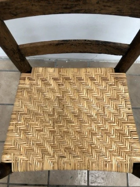 Close-up of a wooden chair with a repaired woven seat, showing the seat and part of the backrest.