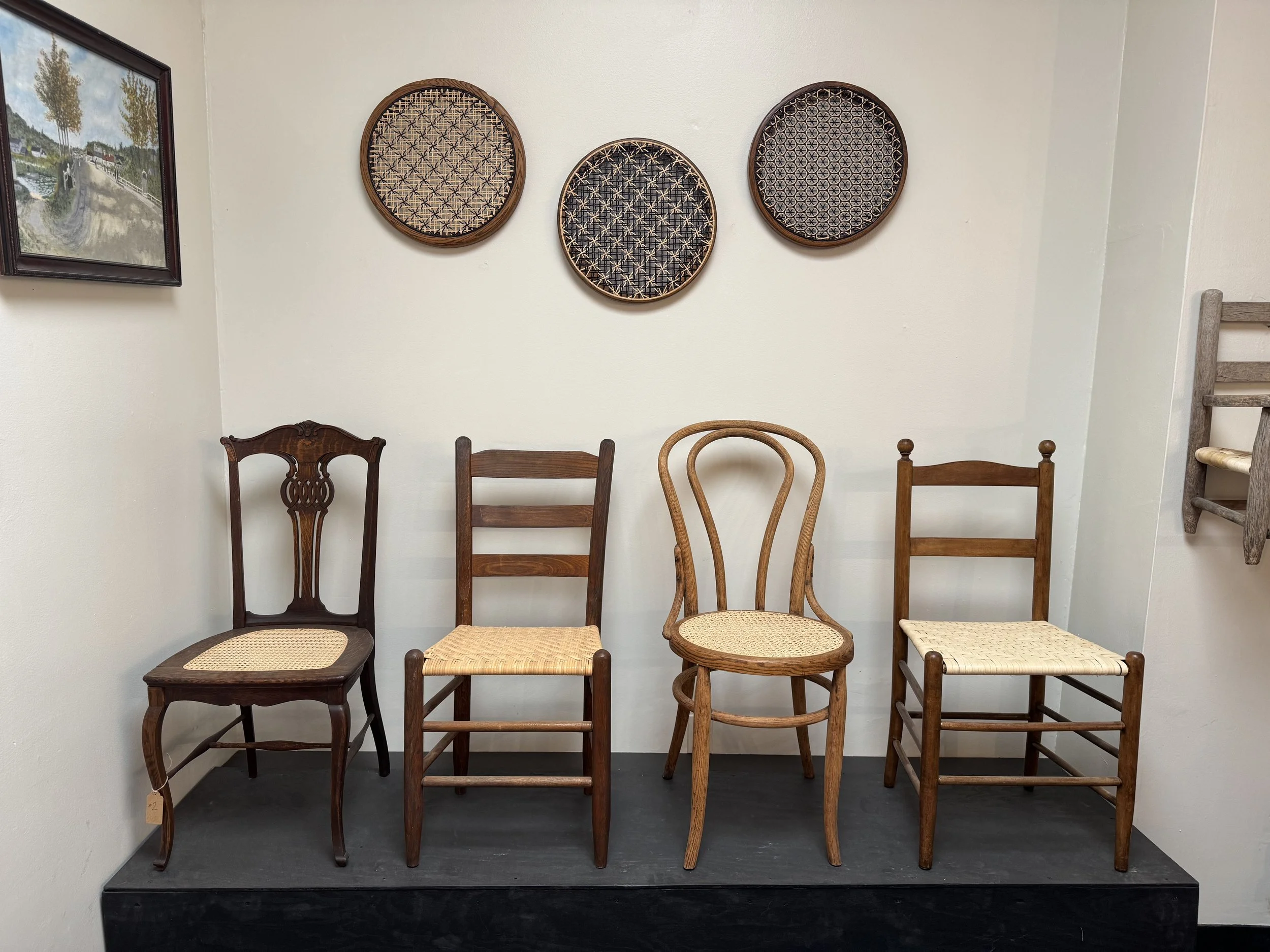 Restored antique chairs with hand-woven seats displayed alongside woven basket trays in Asheville furniture repair studio.