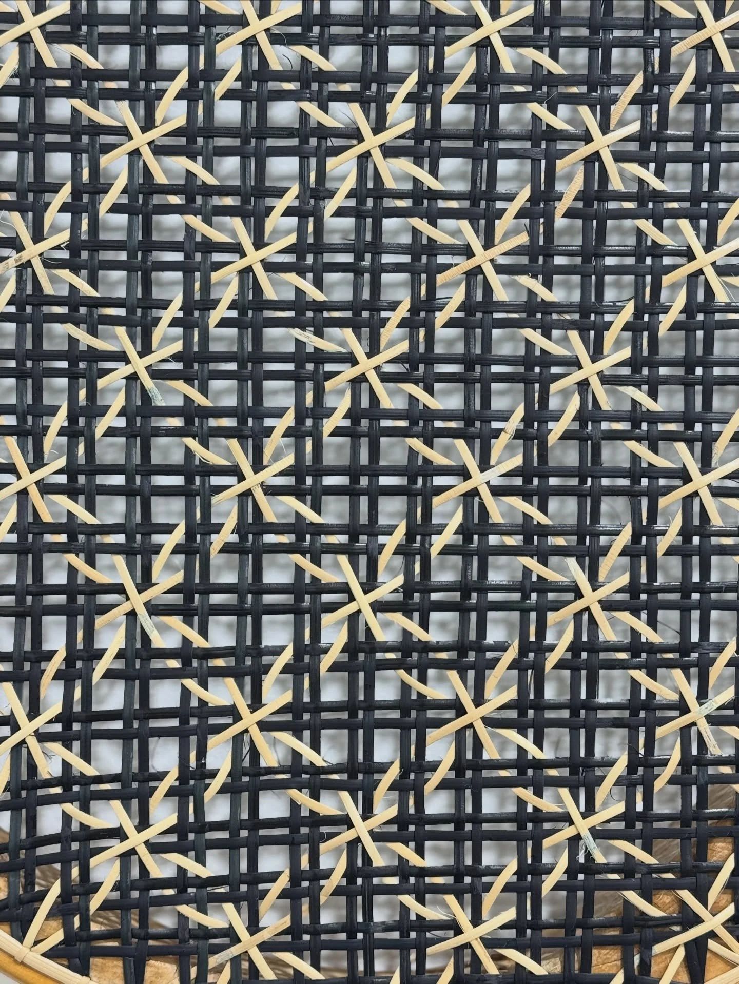 A close-up of a woven rattan or cane chair back with a black and beige pattern.