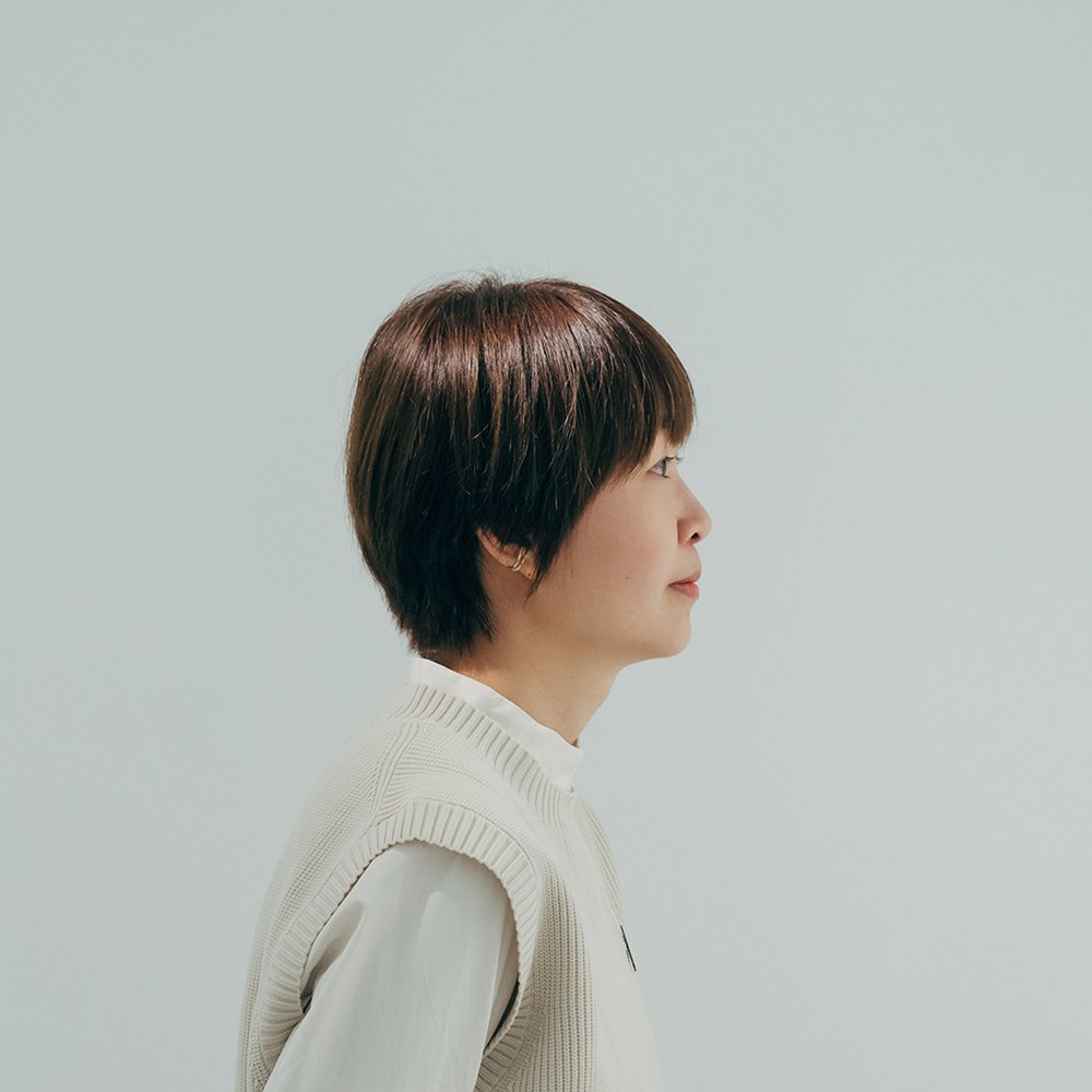 Profile view of a woman with short brown hair wearing a white sweater against a plain light gray background.