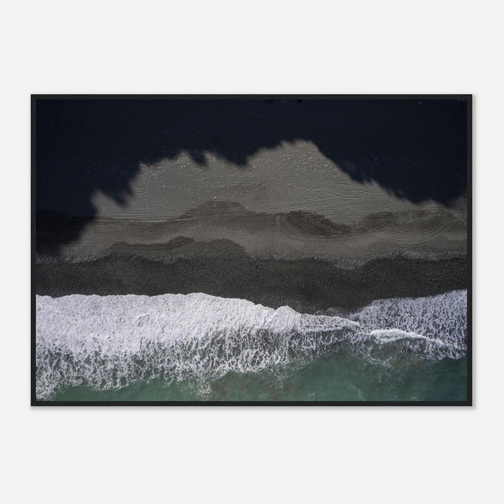 An aerial view of a beach with waves washing onto a dark sandy shore, with shadows from trees cast over part of the beach.