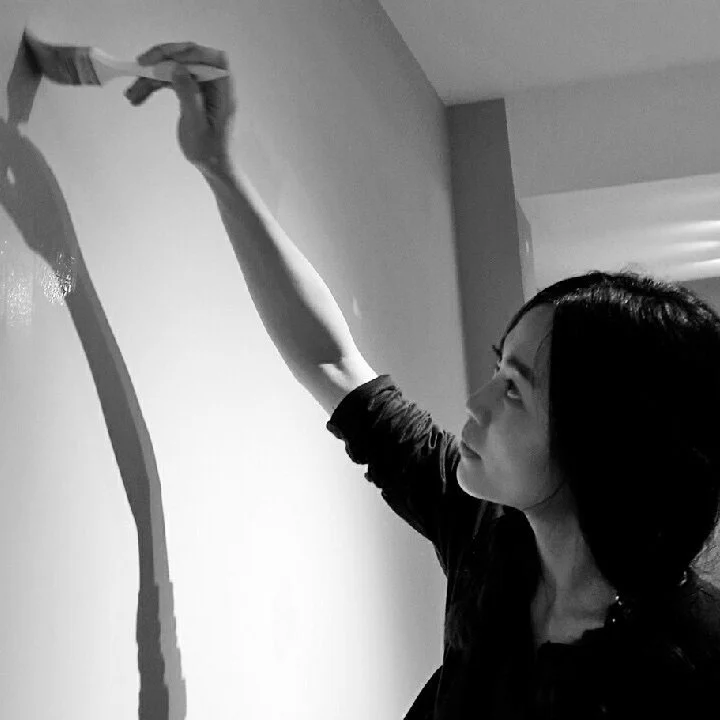 A woman painting a wall with a brush in a black and white photo.