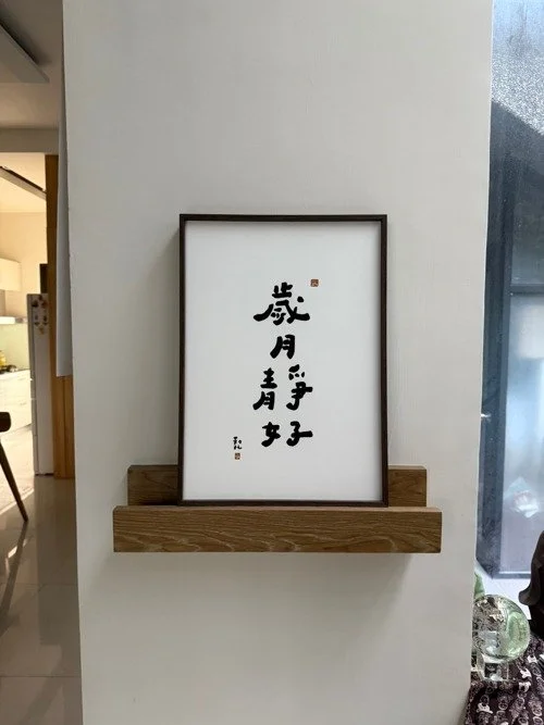 Framed Chinese calligraphy artwork on a wall shelf in a modern interior.