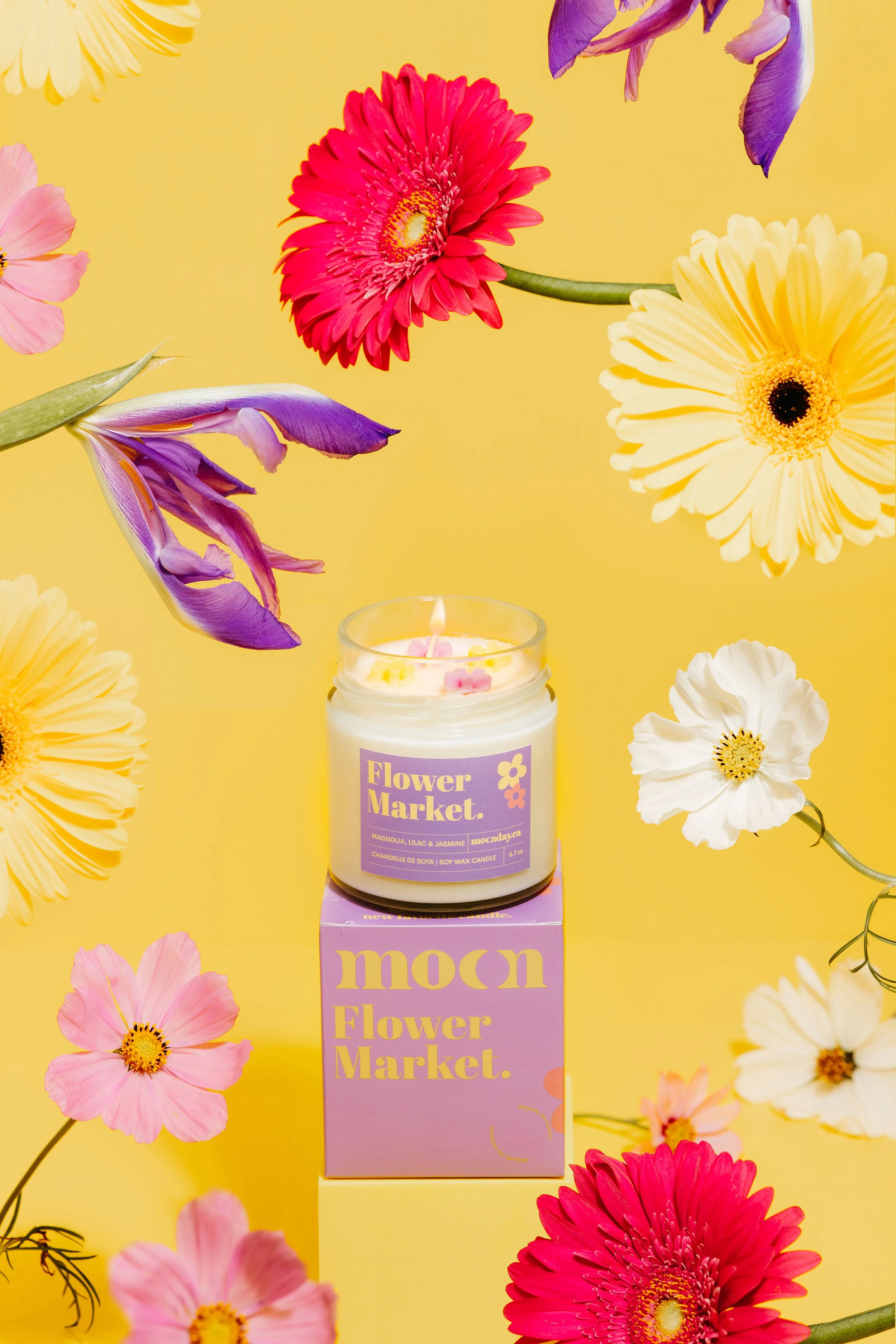 Colorful flowers surrounding a candle on a purple box against a yellow background.