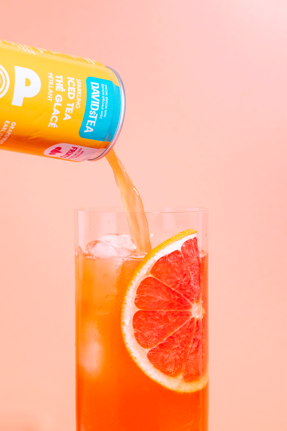 A tall glass of grapefruit iced tea with a slice of grapefruit on the rim, as a can of Davidstea sparkling iced tea is poured into it.