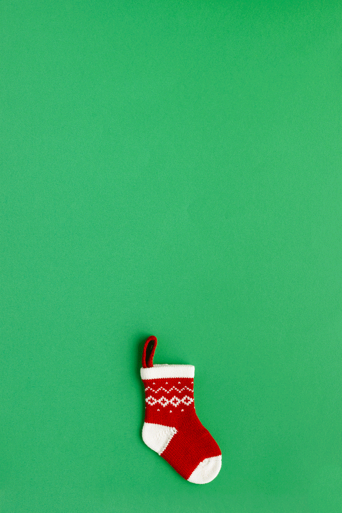 Red and white Christmas stocking with a Christmas pattern, hanging on a green background.