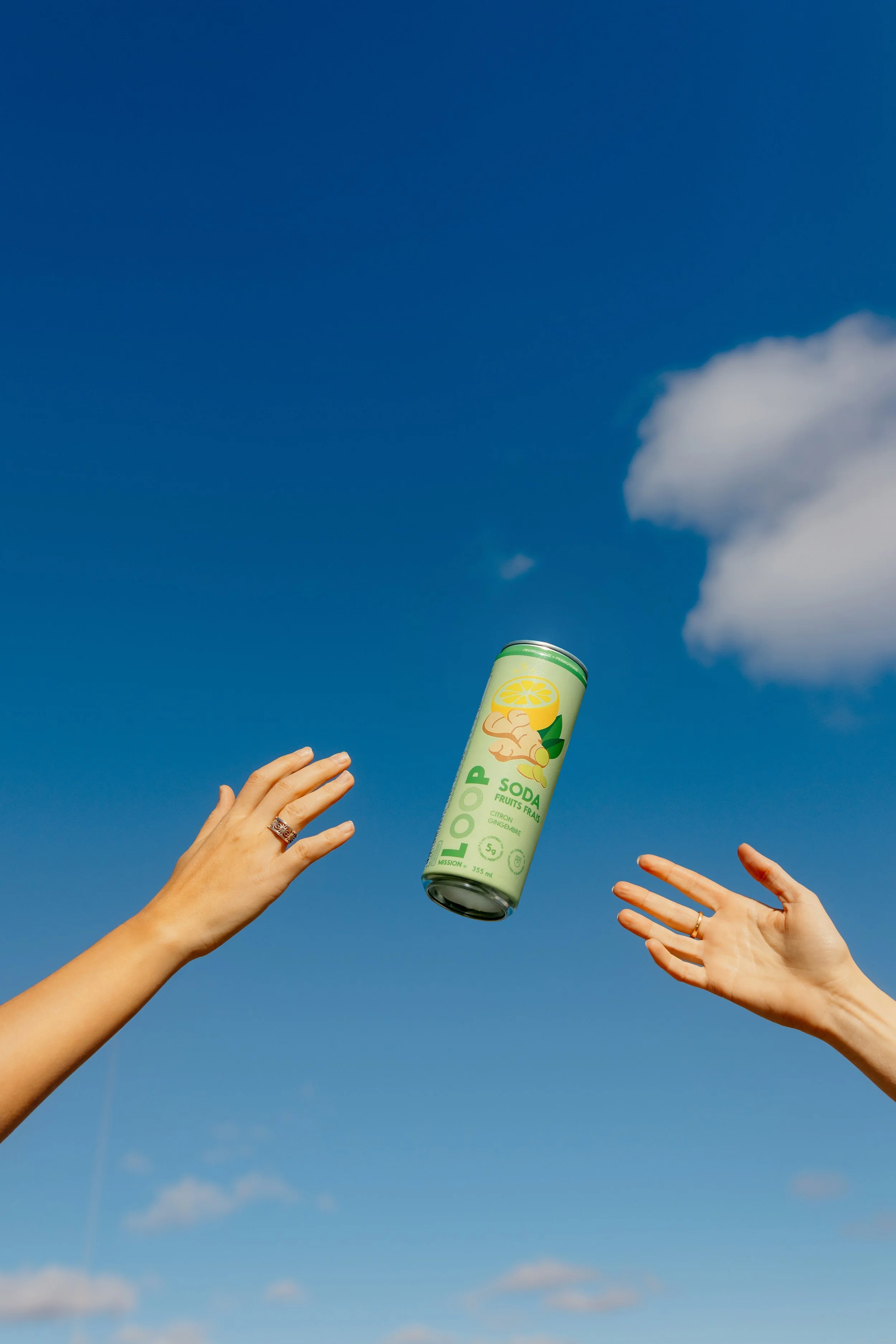 Two hands reaching for a can of Loopp soda in mid-air against a blue sky with a few clouds.