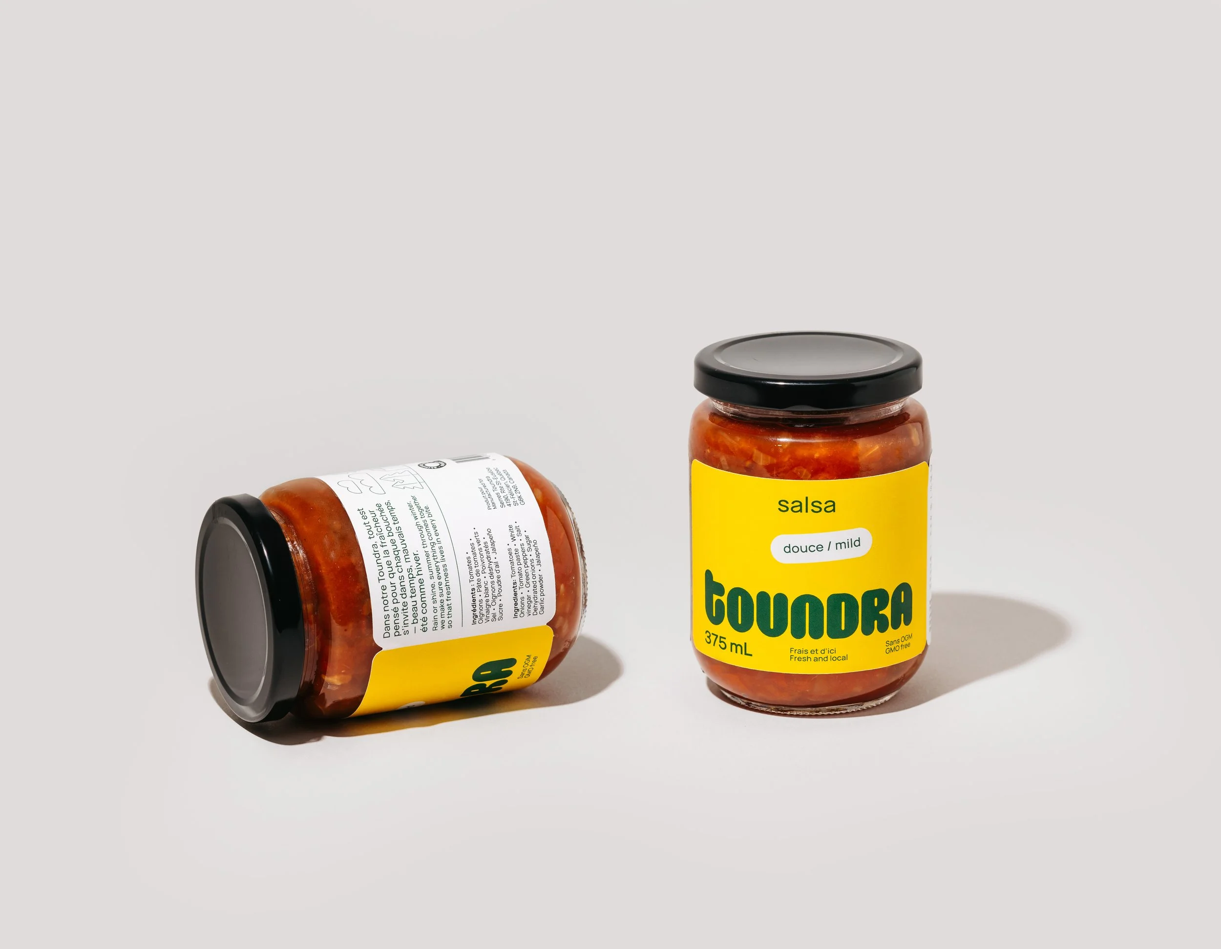Two jars of salsa with yellow labels, one standing upright and one lying on its side against a plain white background.