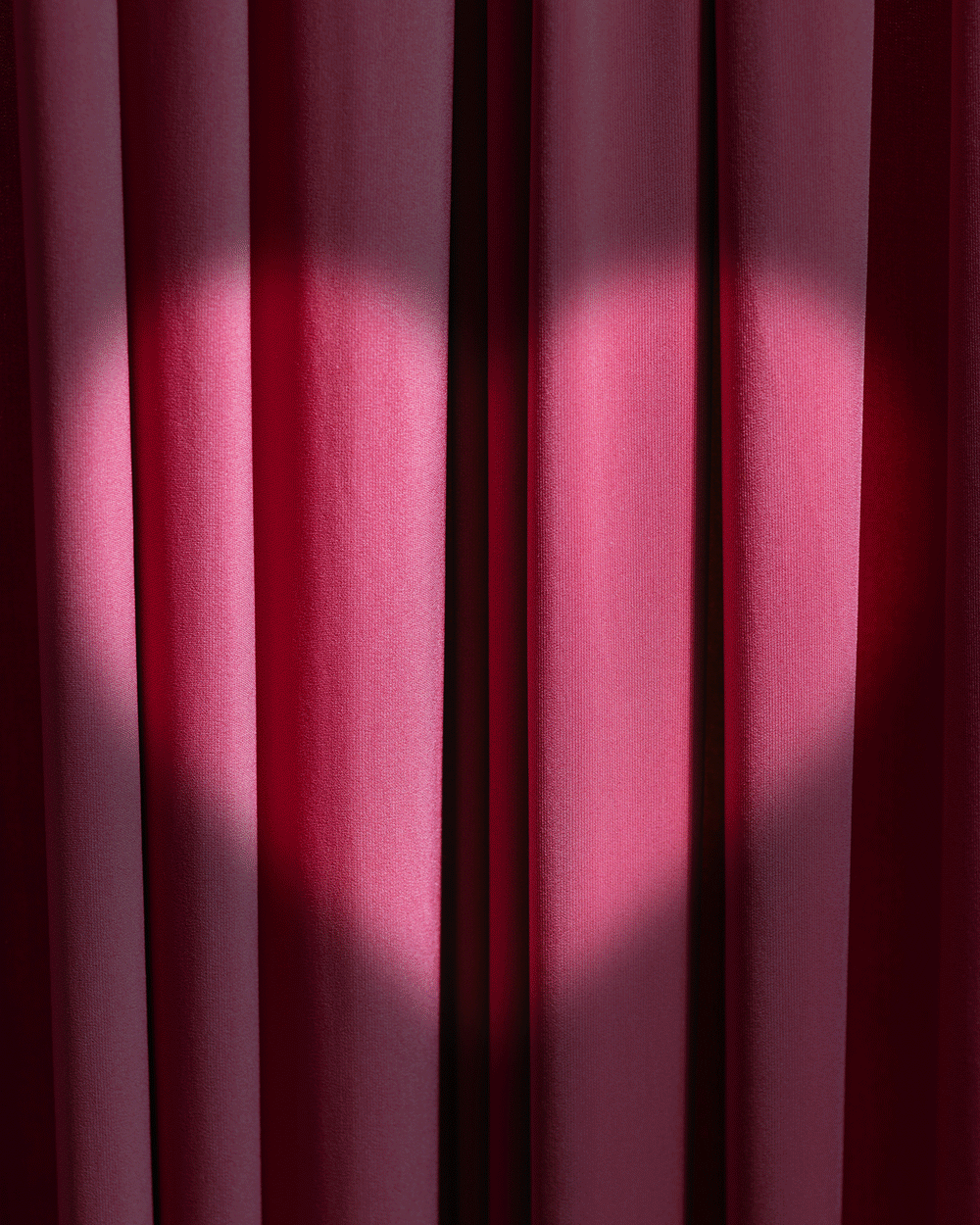 Close-up of pink theater curtain with soft lighting and vertical pleats.