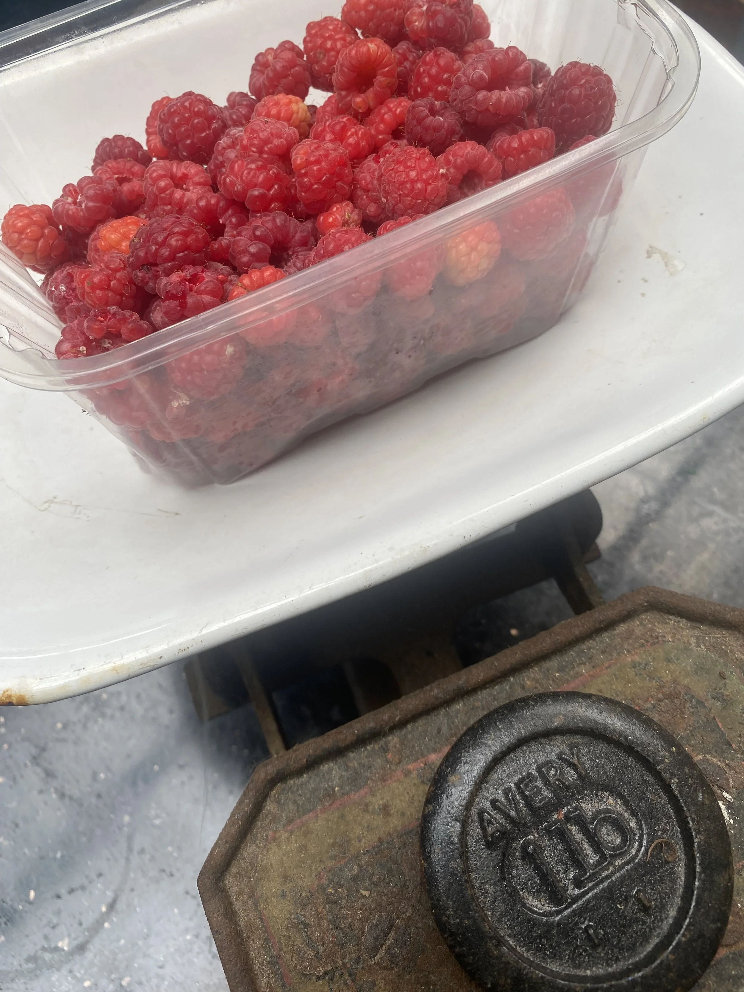 A clear plastic container filled with red raspberries placed on a white surface.