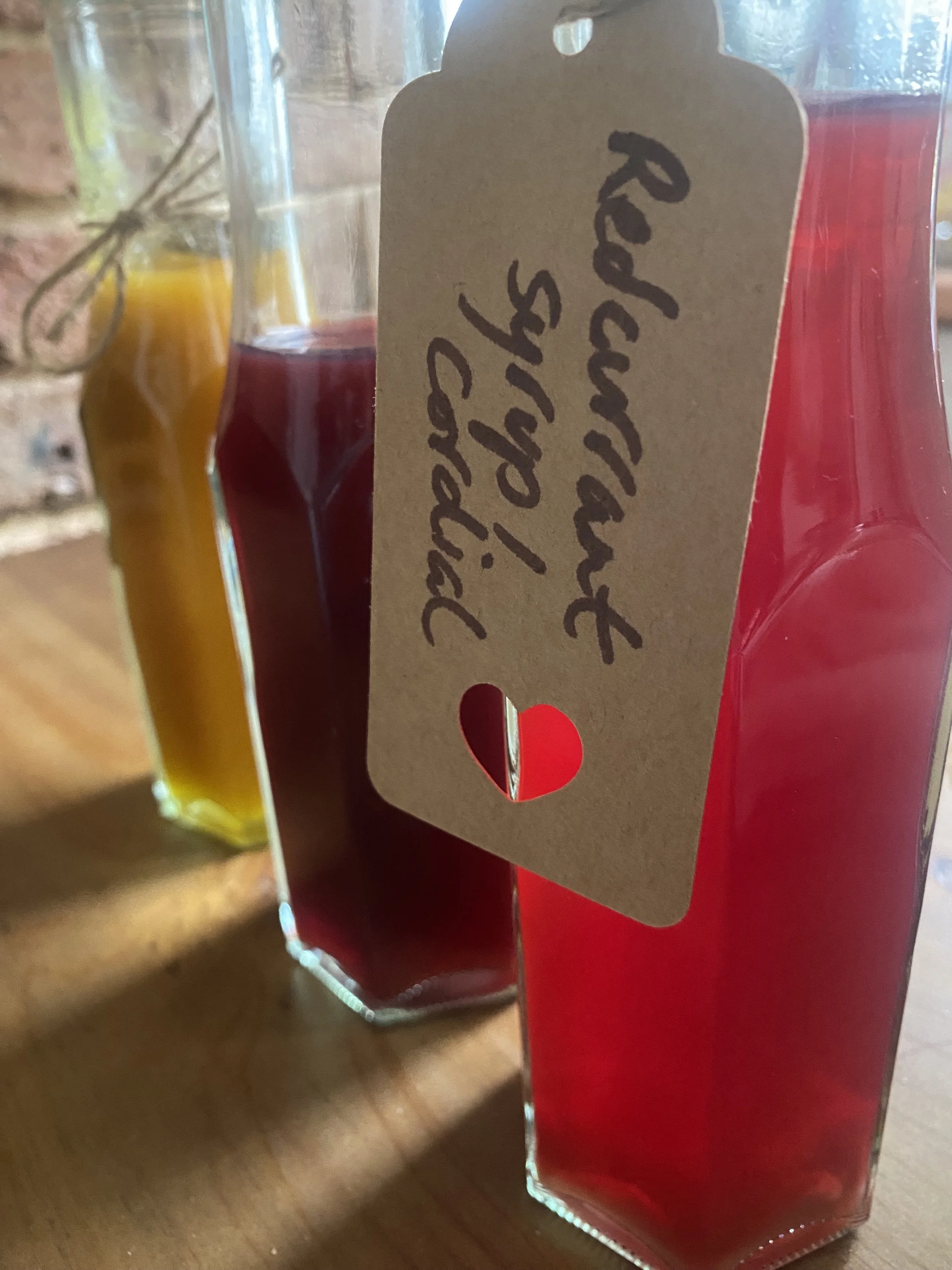 Three glass bottles of various colors, with a beige gift tag reading 'Red, Yellow, & Orange!' hanging from one of the bottles, on a wooden surface.