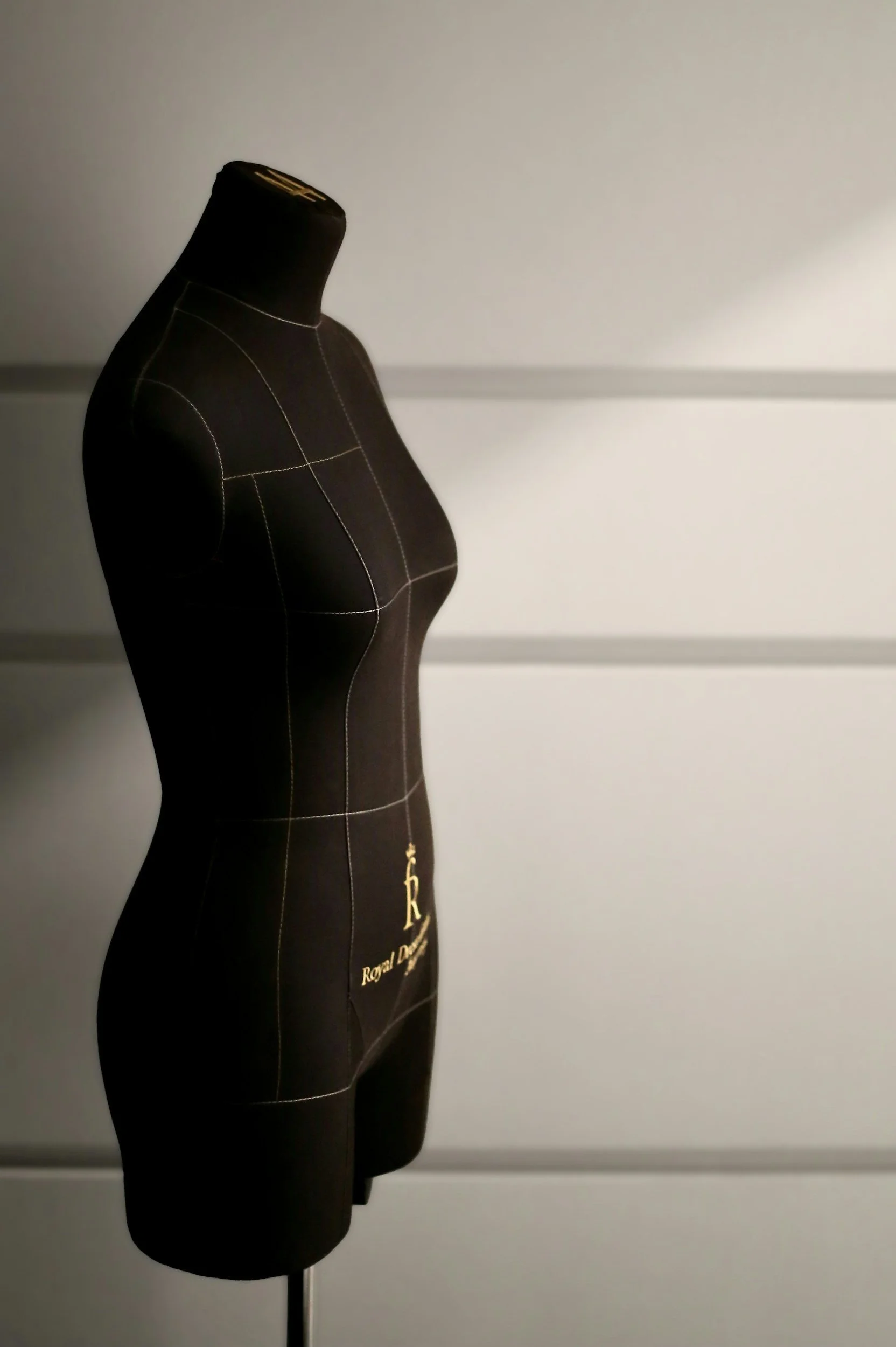 Black dress form mannequin with yellow stitching, featuring gold logo reading "Royal Dress" against a plain wall.