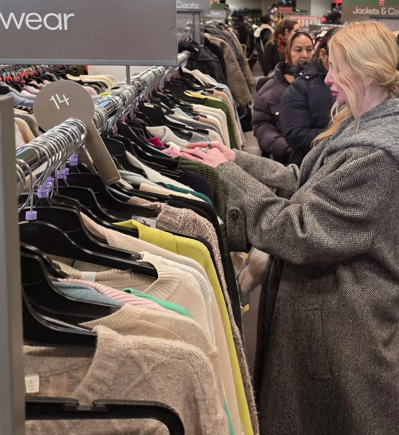 People shopping for sweaters at a clothing store, some browsing and some examining items.