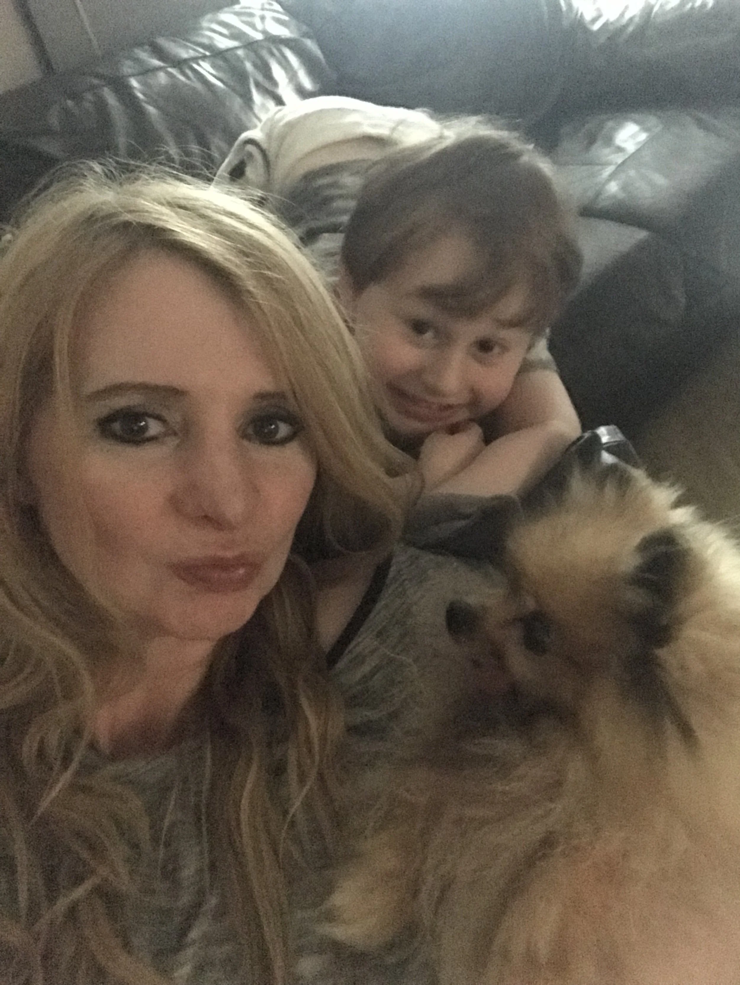 A woman, a young boy, and a dog lying on a couch for a selfie.