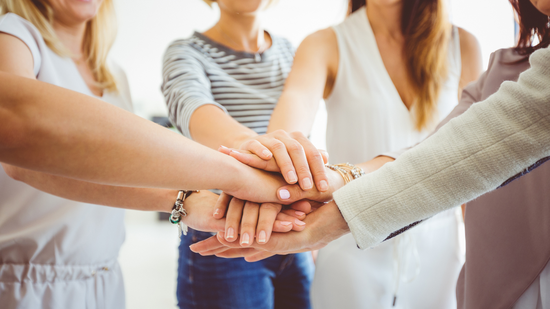 Multiple women stacking their hands together in a team huddle.