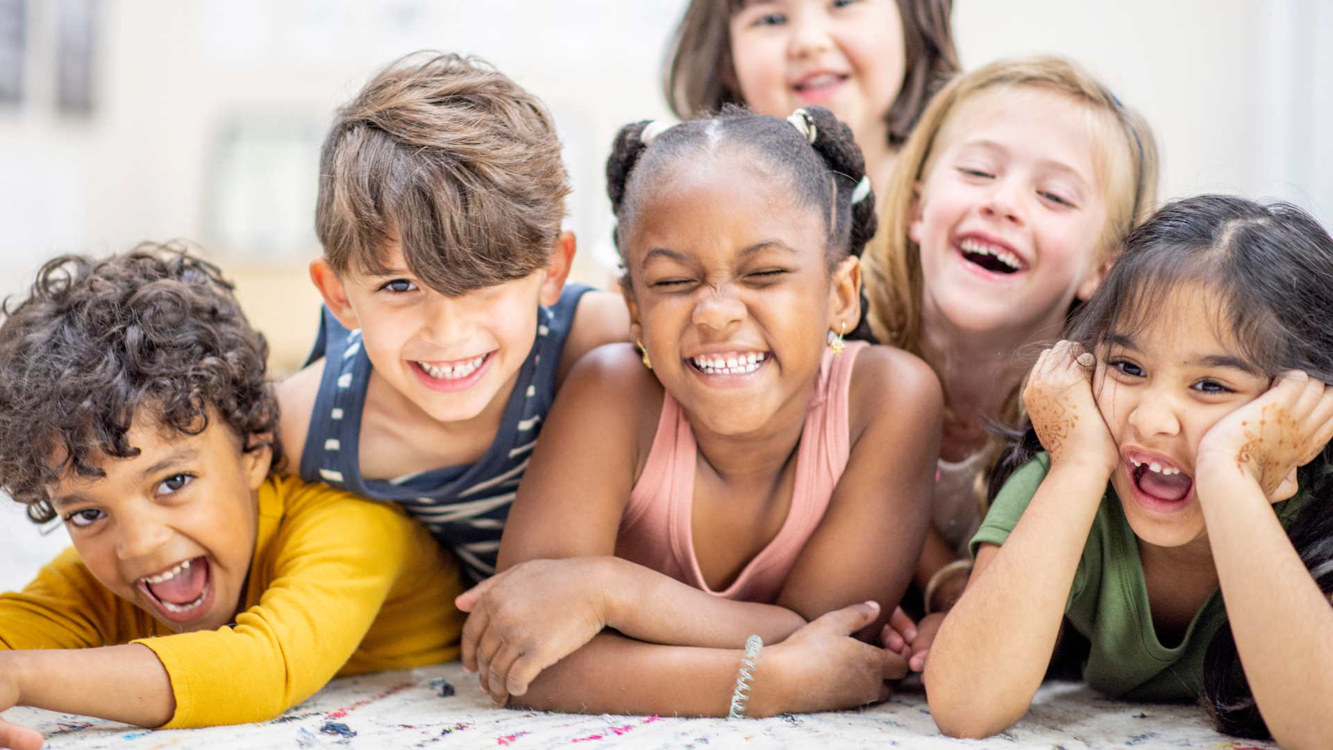A diverse group of six children lying on the floor and smiling.