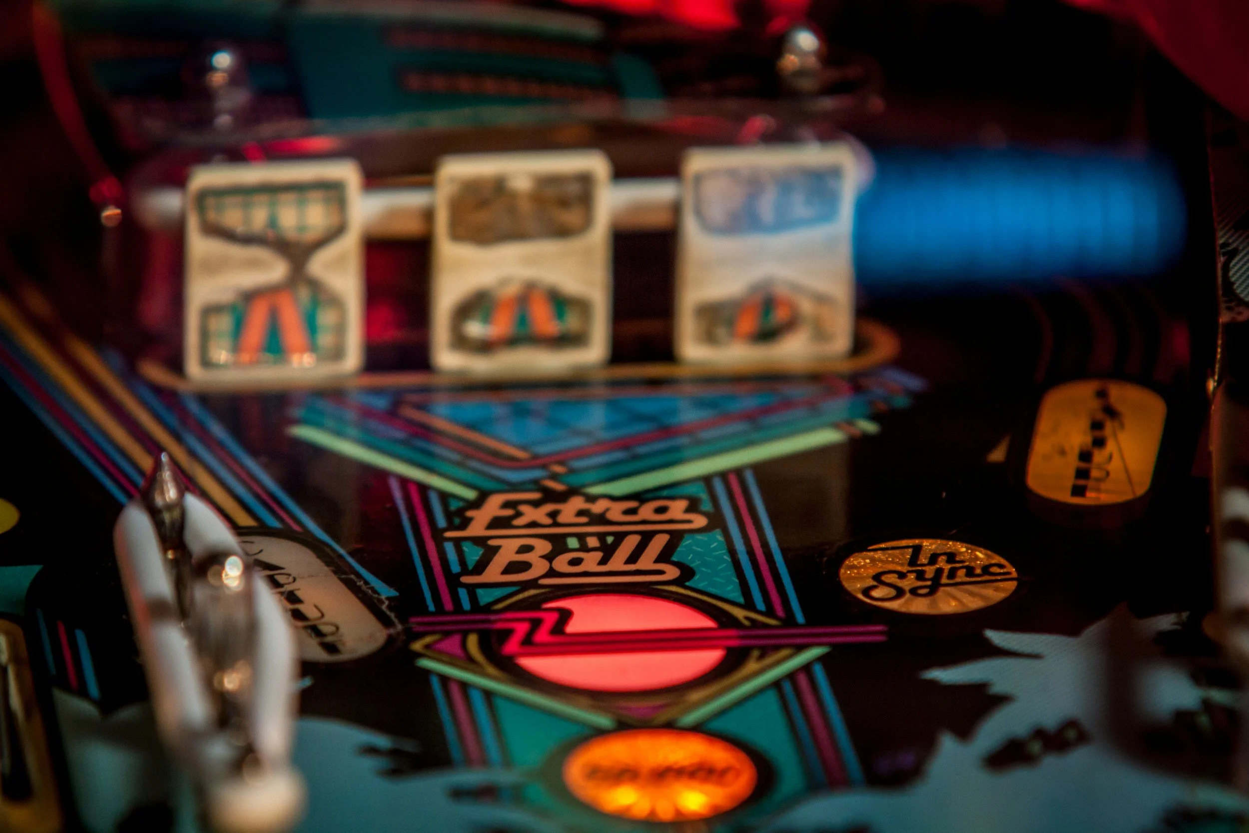 Close-up of a colorful pinball machine playing field, featuring bumpers, flashing lights, and the words 'Extra Ball'.