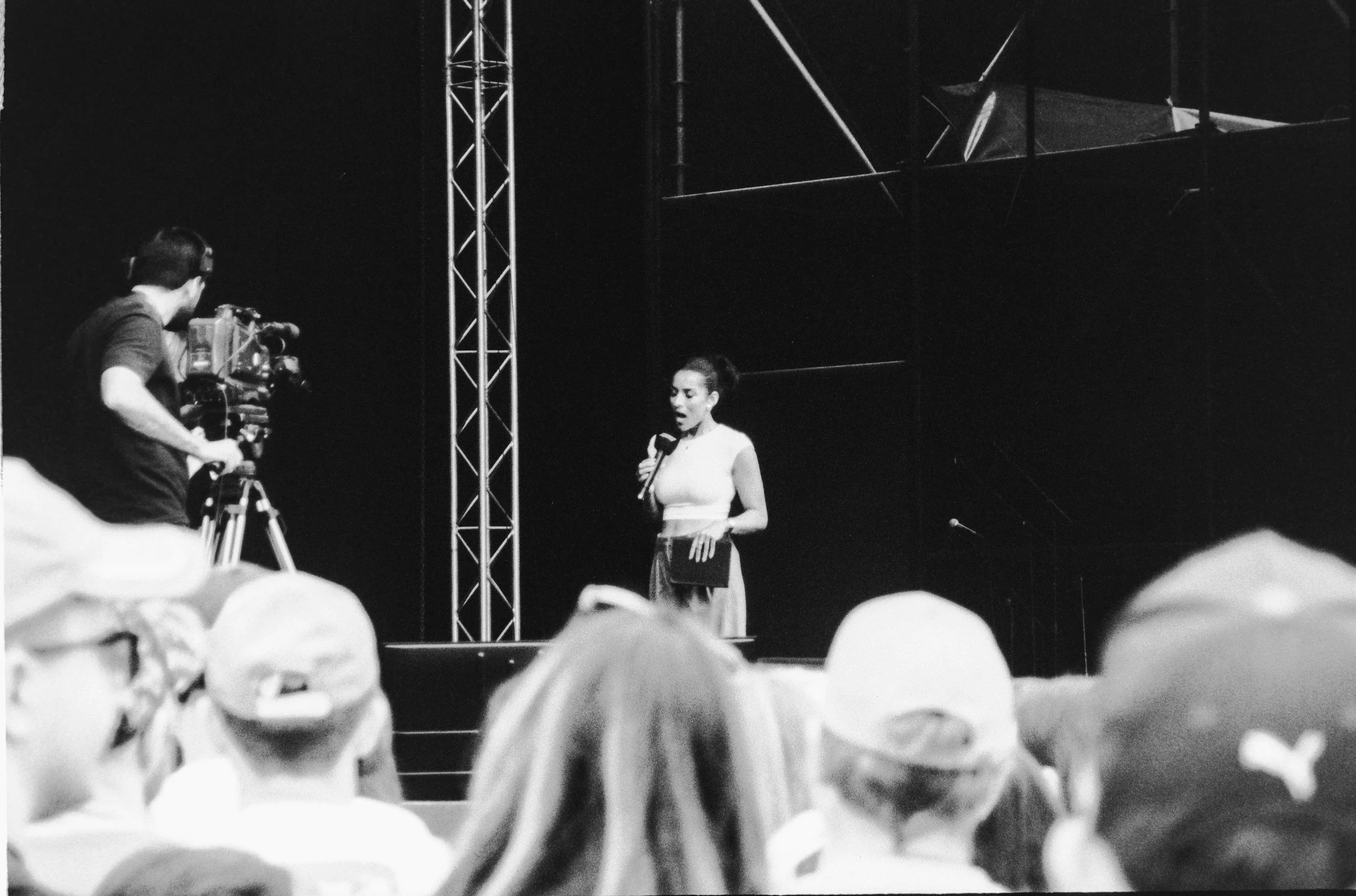A female speaker holding a microphone in front of a large audience during a presentation.