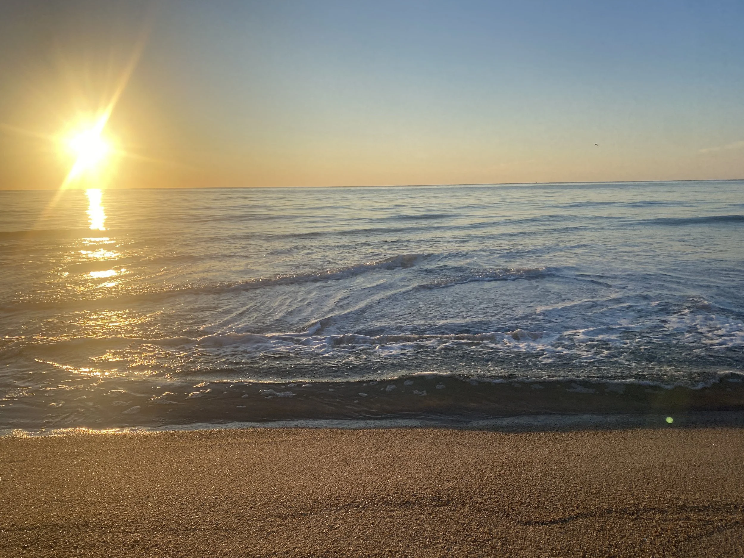 Sunset over the ocean with gentle waves hitting the sandy beach.