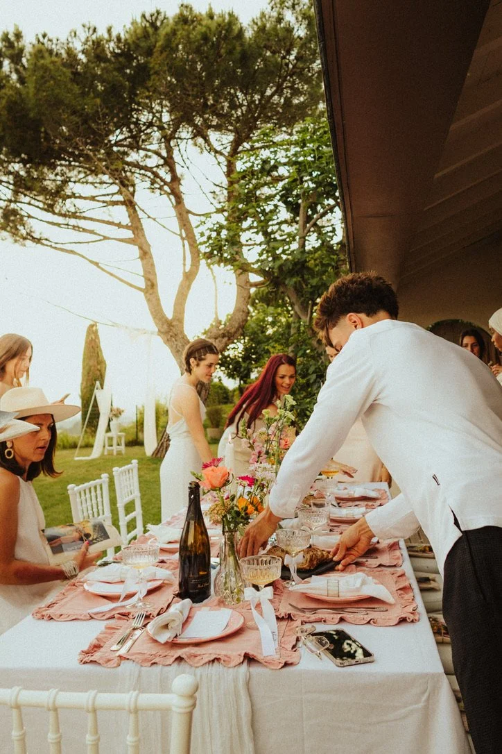 Célébration d'un dîner en plein air avec un groupe de personnes, tables décorées avec des fleurs, à l'extérieur, entourées d'arbres.