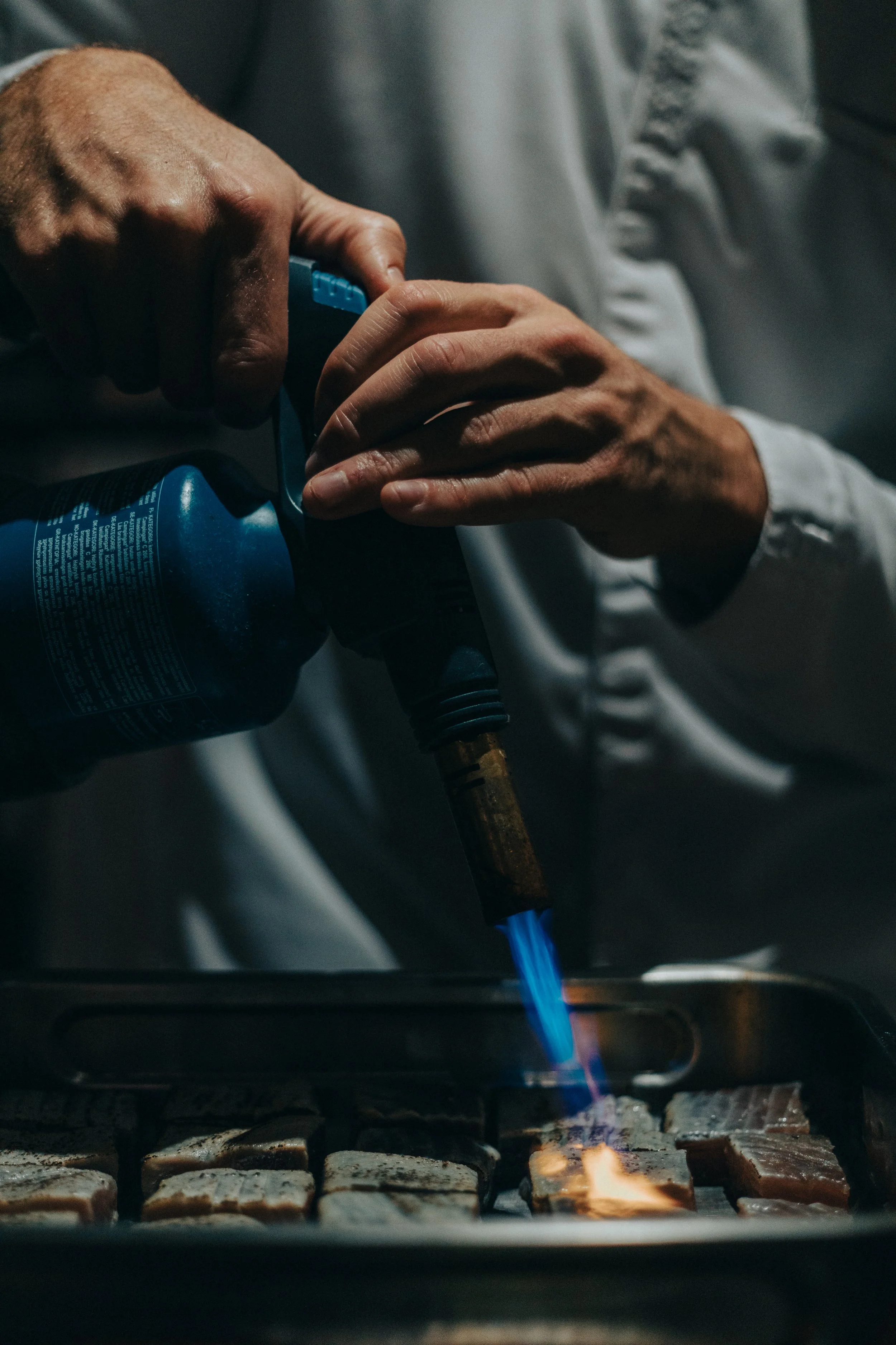 Une personne utilise un chalumeau pour caraméliser la surface de cassonade sur des toasts dans un four.