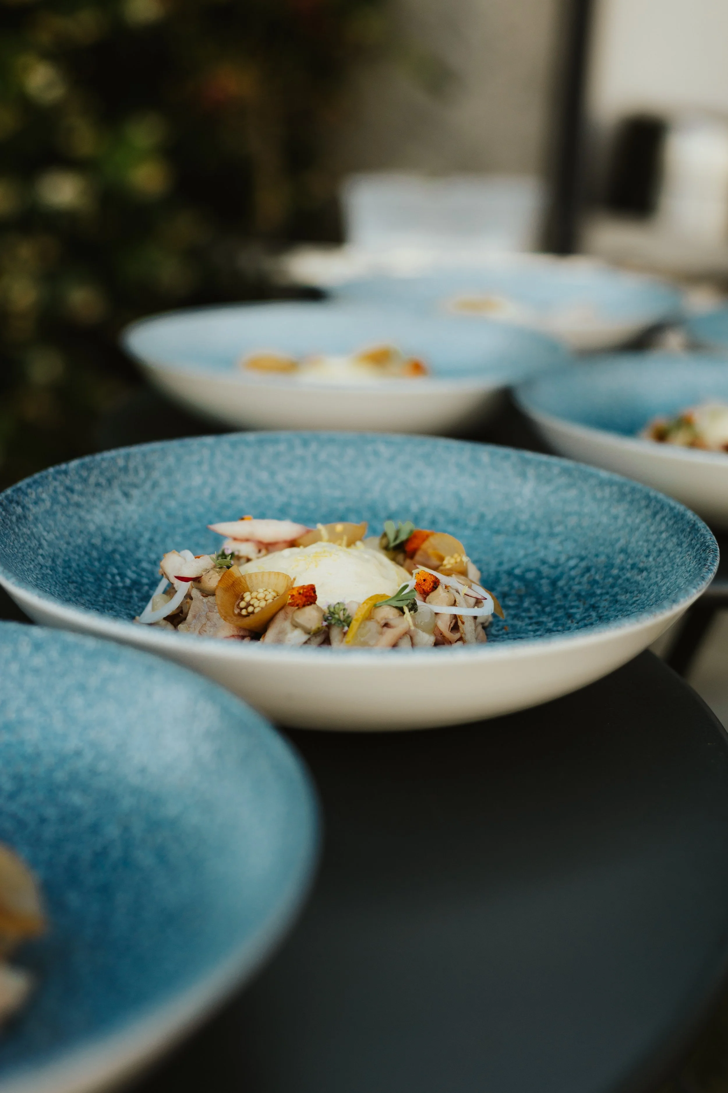Assiette de nourriture fraîche avec œuf poché, légumes et herbes dans un bol bleu, plusieurs assiettes similaires en arrière-plan.