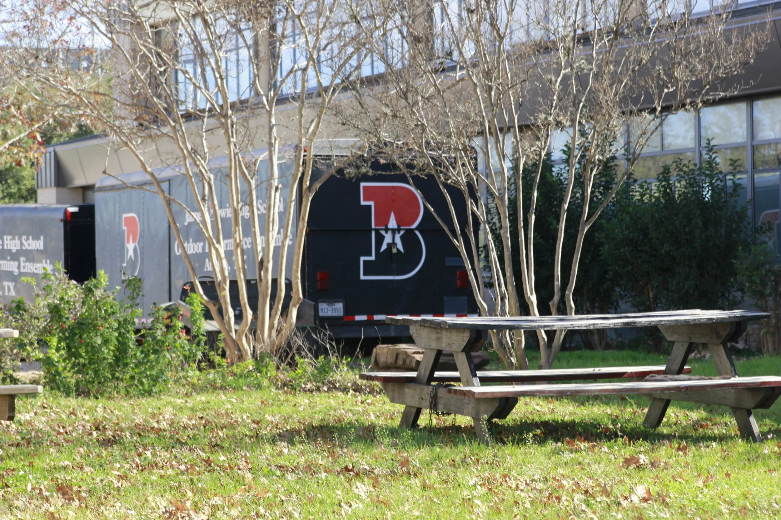Tree and bushes in front of a building with a large trailer that has a red, black, and white logo and text.