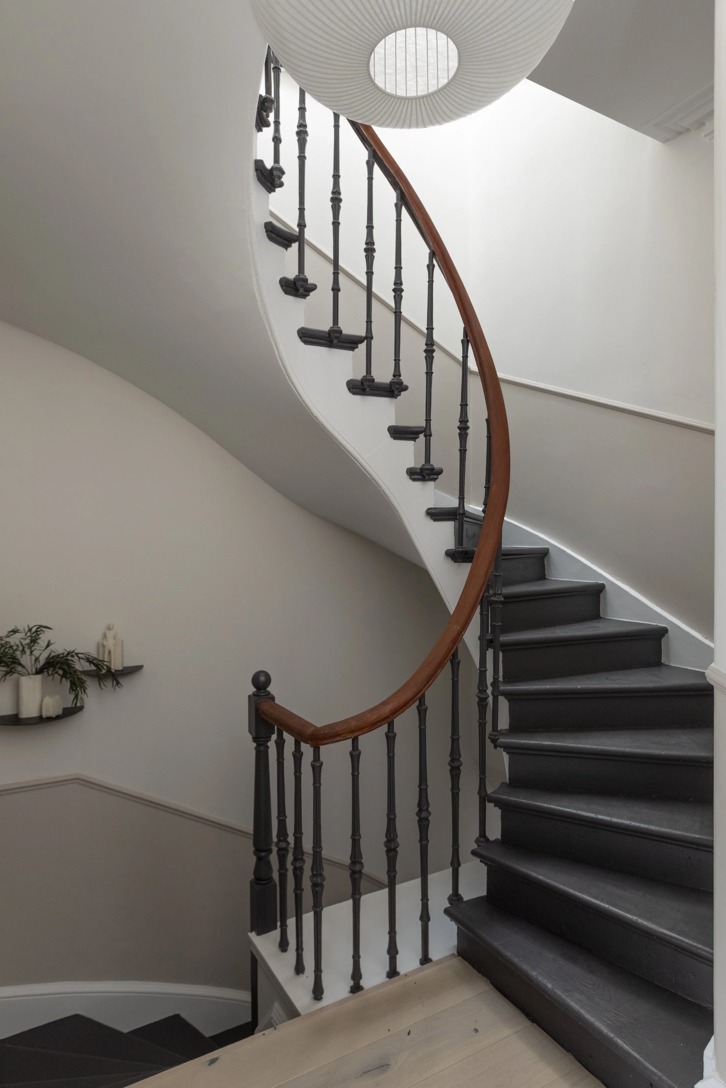 A staircase with black steps, black spindles, and a wooden handrail, curved along a white wall in a modern interior.