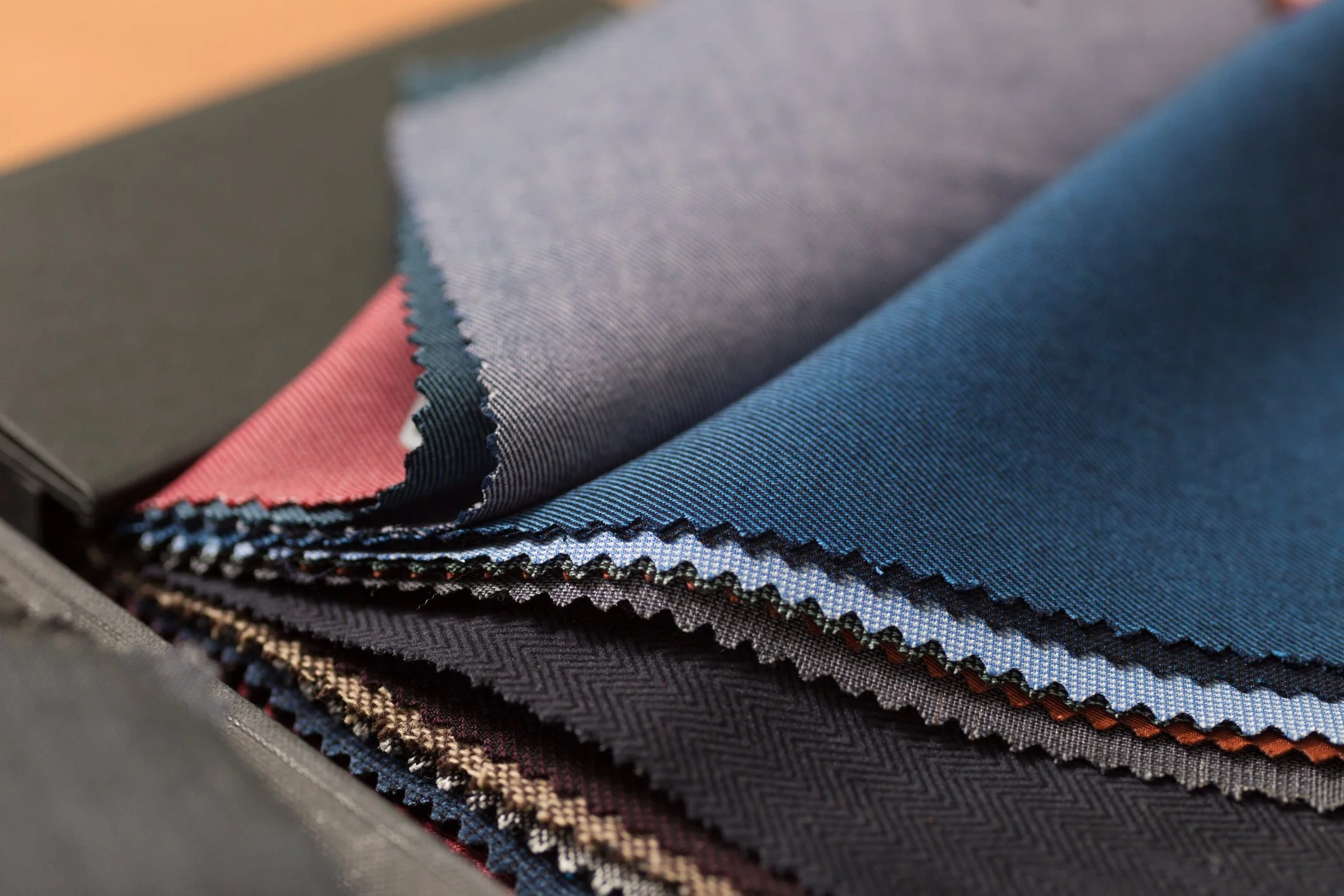 Stacked fabric swatches in various colors and textures, including blue, gray, black, and red, arranged in a fan shape.