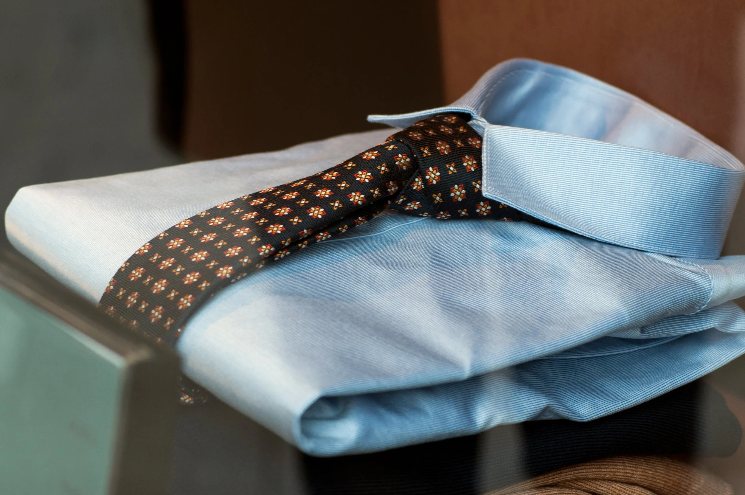 A light blue collared dress shirt with a patterned black tie draped over it.