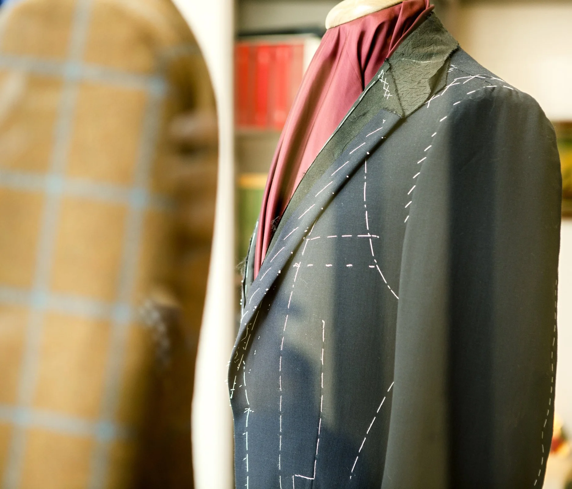 A tailored black suit jacket on a mannequin, with pattern markings visible, displayed in a tailor's workshop.