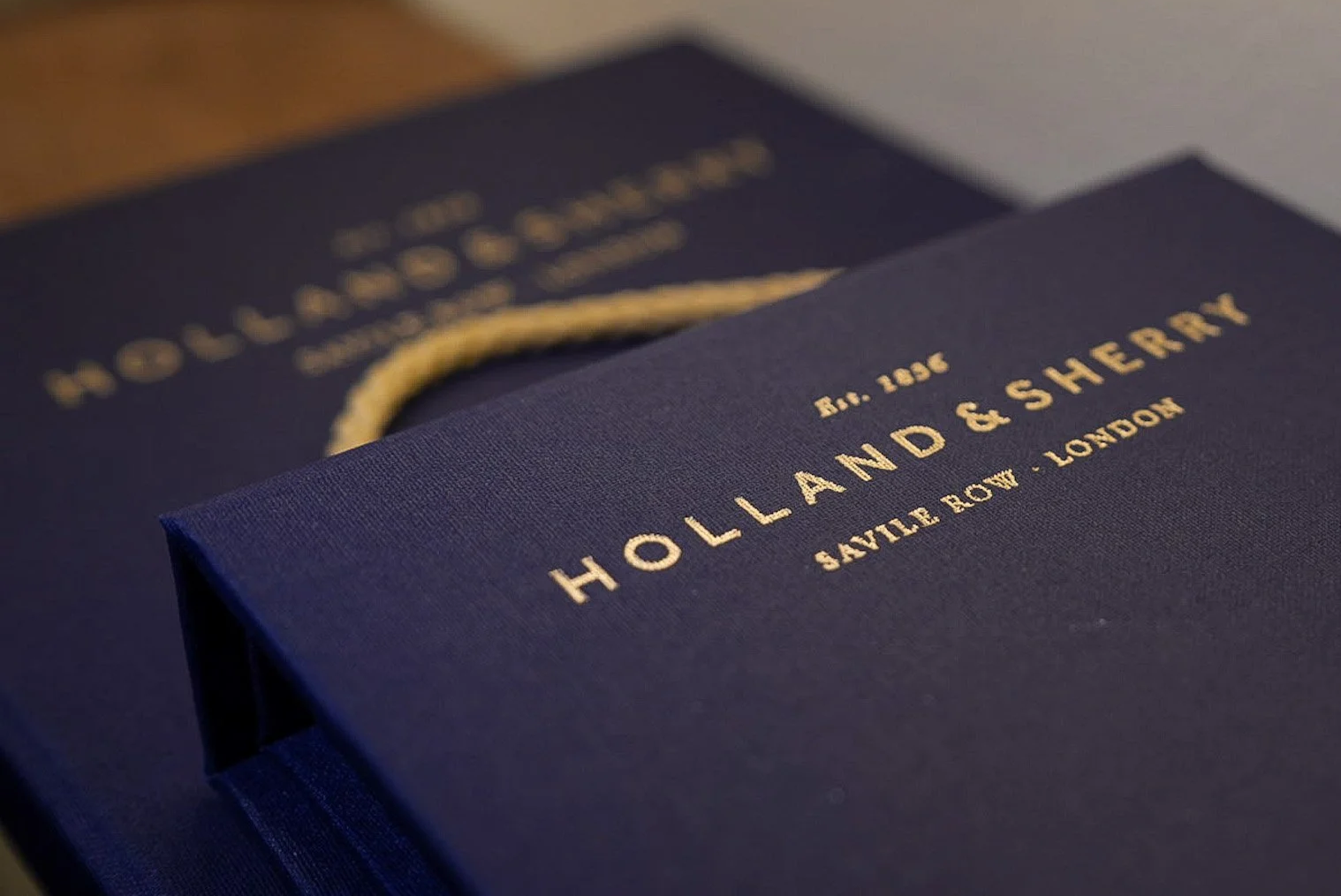 Close-up of navy blue shopping bags with gold embossed text reading "HOLLAND & SHERRY" and "SAVILE ROW, LONDON".