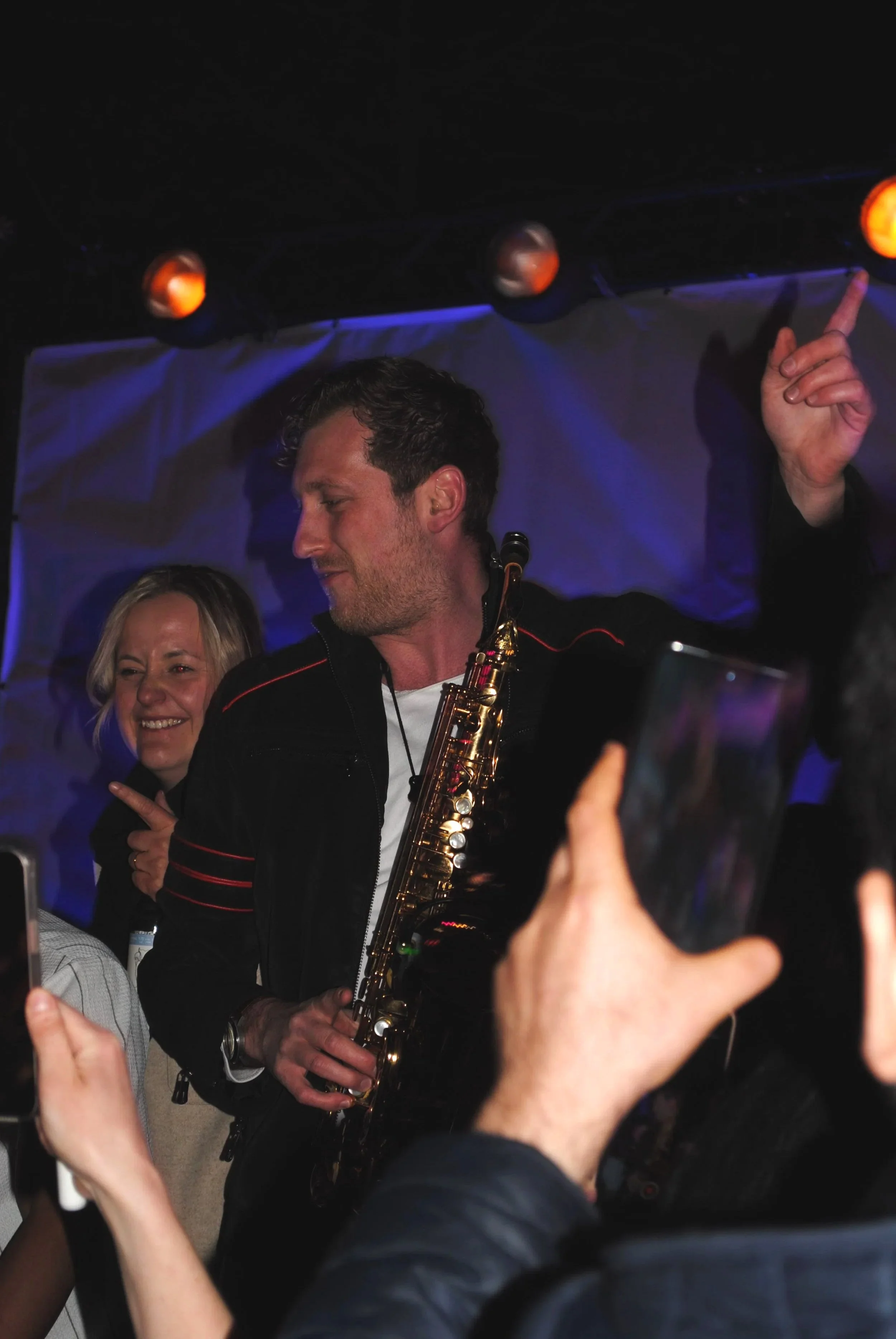 Frederik Heckel mit Saxophon bei einer Live-Performance, umgeben von jubelnden Publikum und unterwegs auf der Bühne, mit dunkler Beleuchtung und bunten Lichtern.