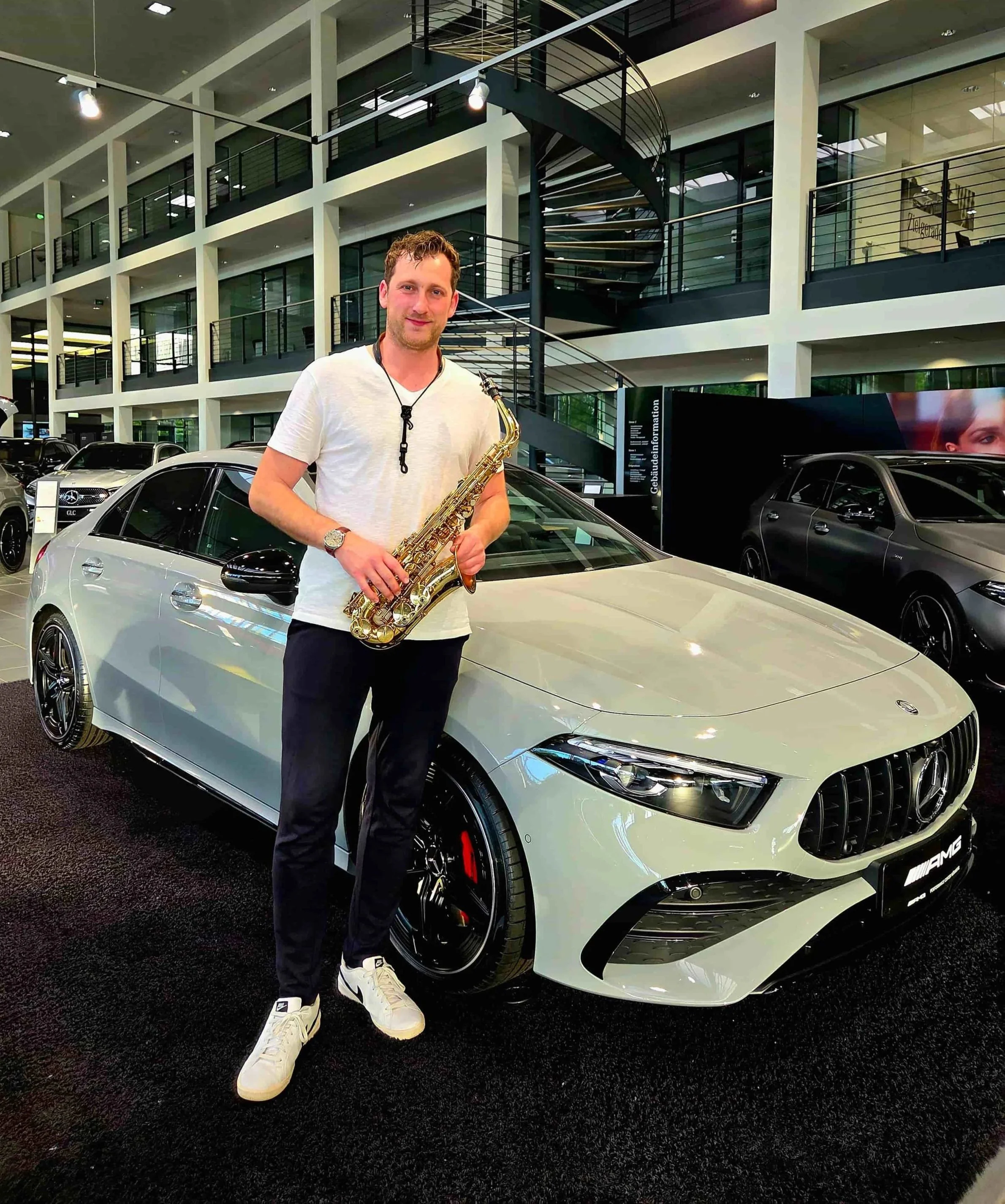 Frederik Heckel mit Saxophon vor einem weißen Mercedes-Benz und einem Autohaus